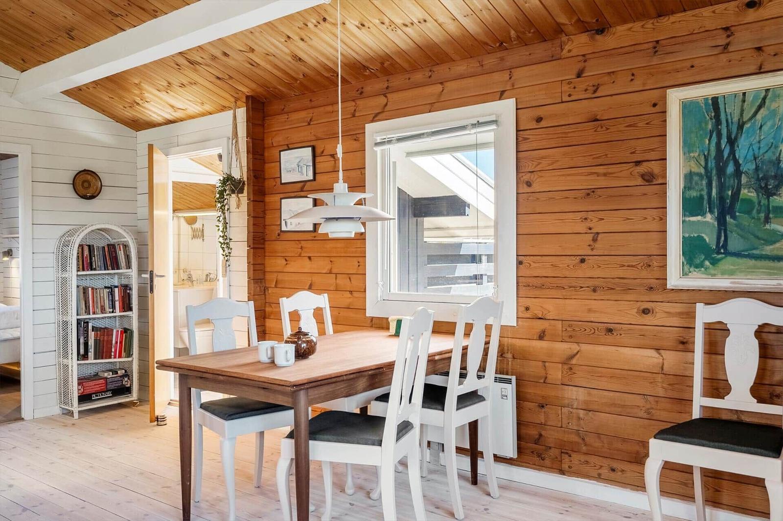Essbereich mit Holzwand, Tisch und Stühlen. Fenster und Bild an der Wand.