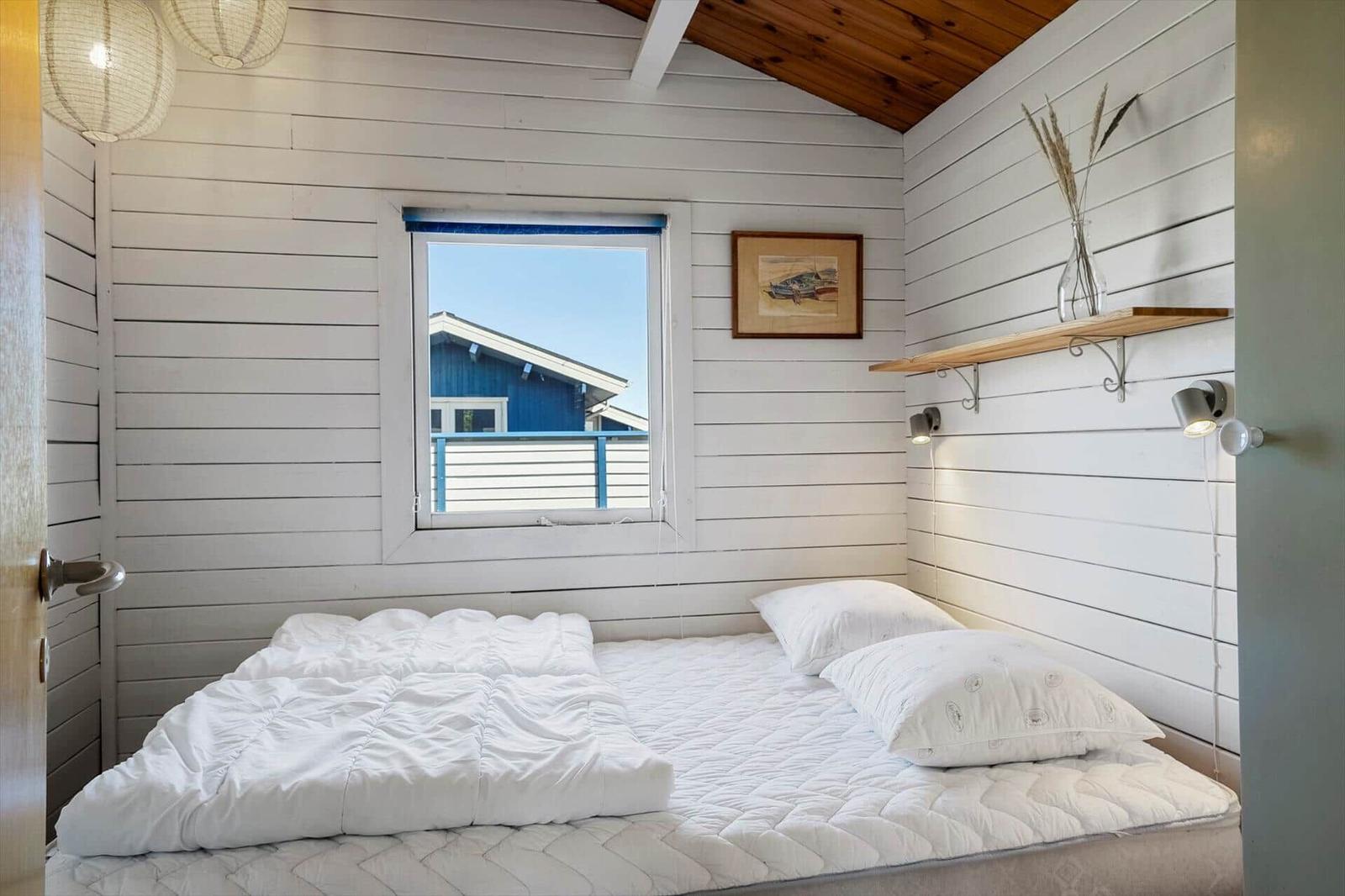 Schlafzimmer mit weißem Bett, Fenster und Holzwand. Decke mit Holzverkleidung.