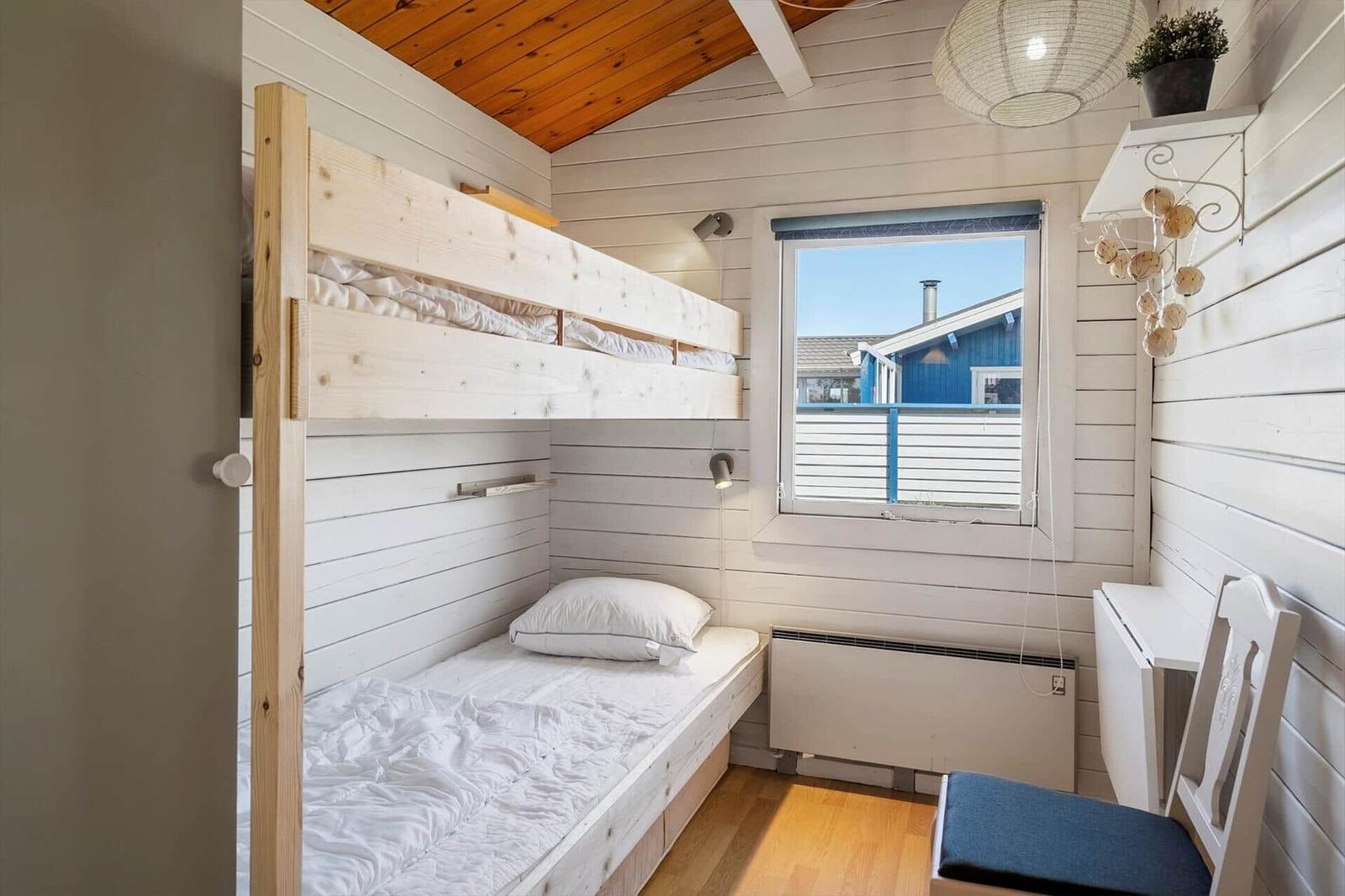 Zimmer mit Doppelstockbett, Fenster und Stuhl. Holzdecke und weiße Wände.