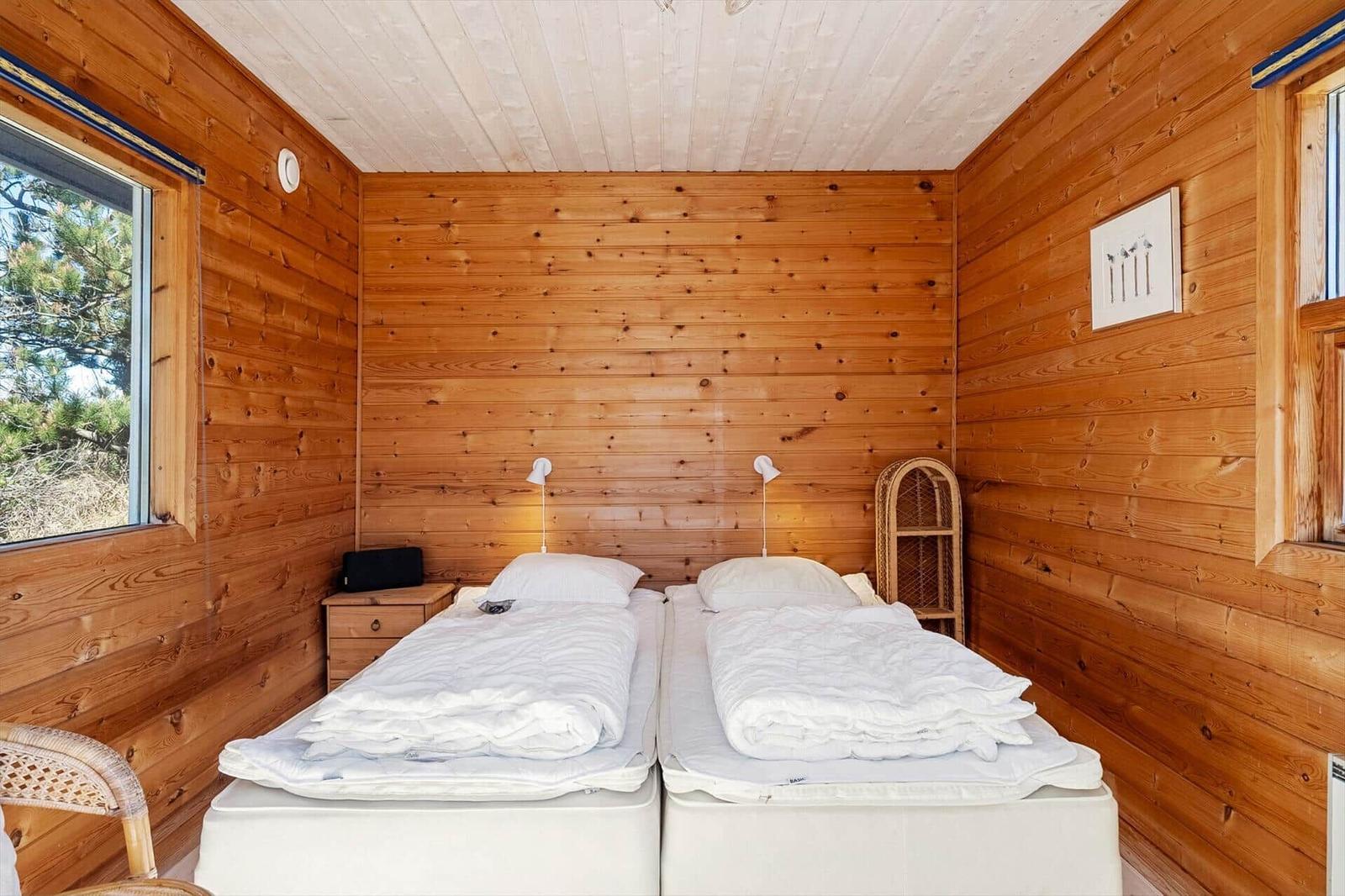 Zwei Betten mit weißen Bettwäschen in einem Holzhauszimmer mit Fenstern.