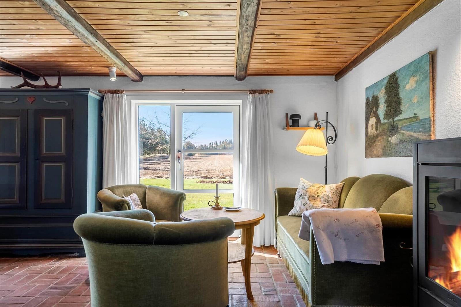 Living room with fireplace, green chairs, and view of fields.