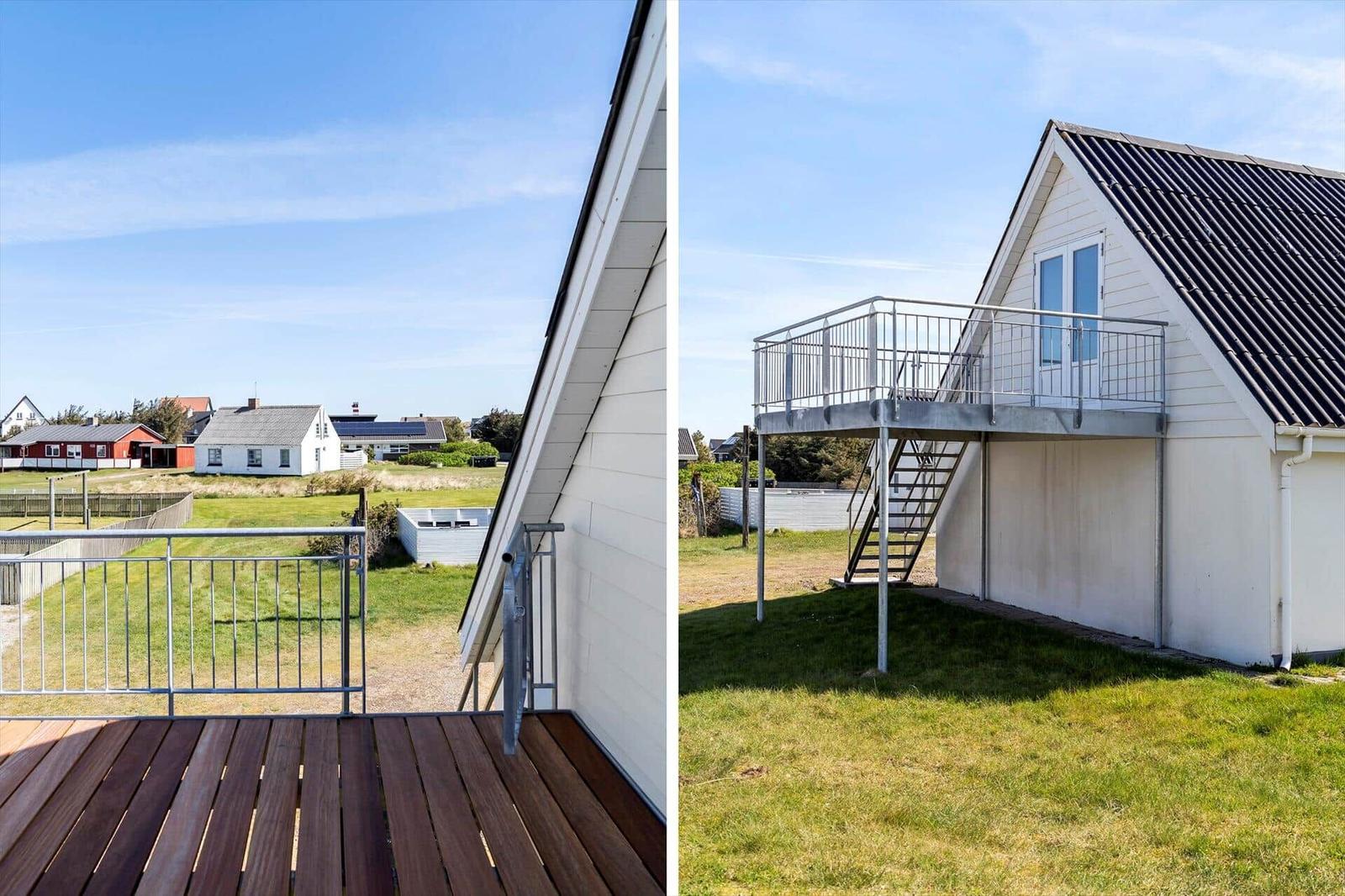 Terrasse mit Holzdielen und Blick auf das Grasland. Metallgeländer und Treppenhaus zur oberen Terrasse.