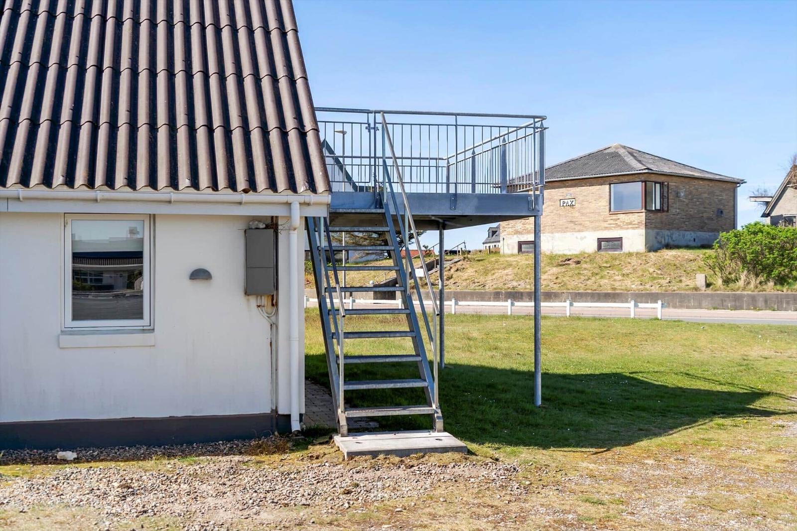 Haus mit Metalltreppe und Balkon, Grasfläche und Nachbarhaus im Hintergrund.