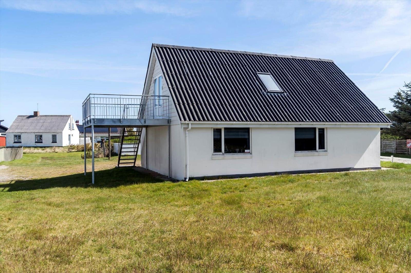 Ein weißes Haus mit schwarzem Dach und Balkon. Grasland im Vordergrund.