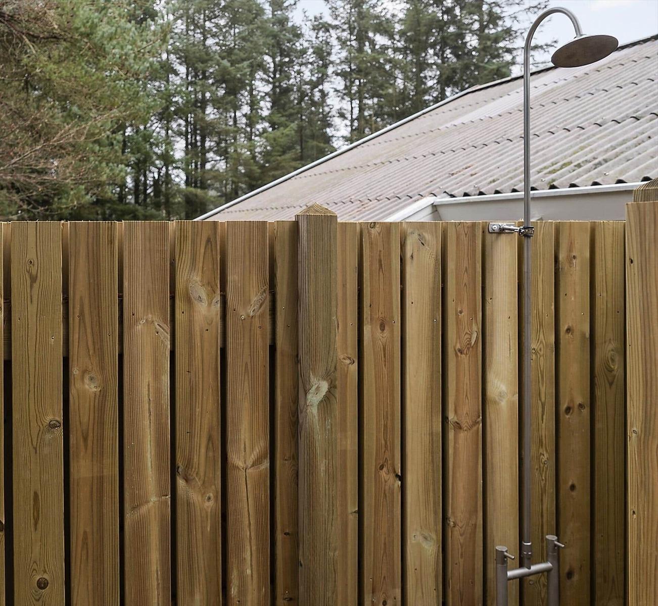 Außenbereich mit Holzzaun und Duschinstallation. Hintergrund: Dach und Wald.