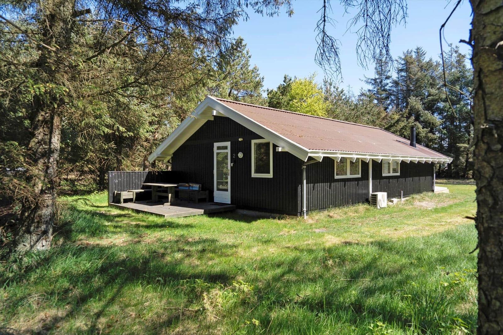 Schwarze Holzhütte mit Terrasse, Tisch und Stühlen im Wald.