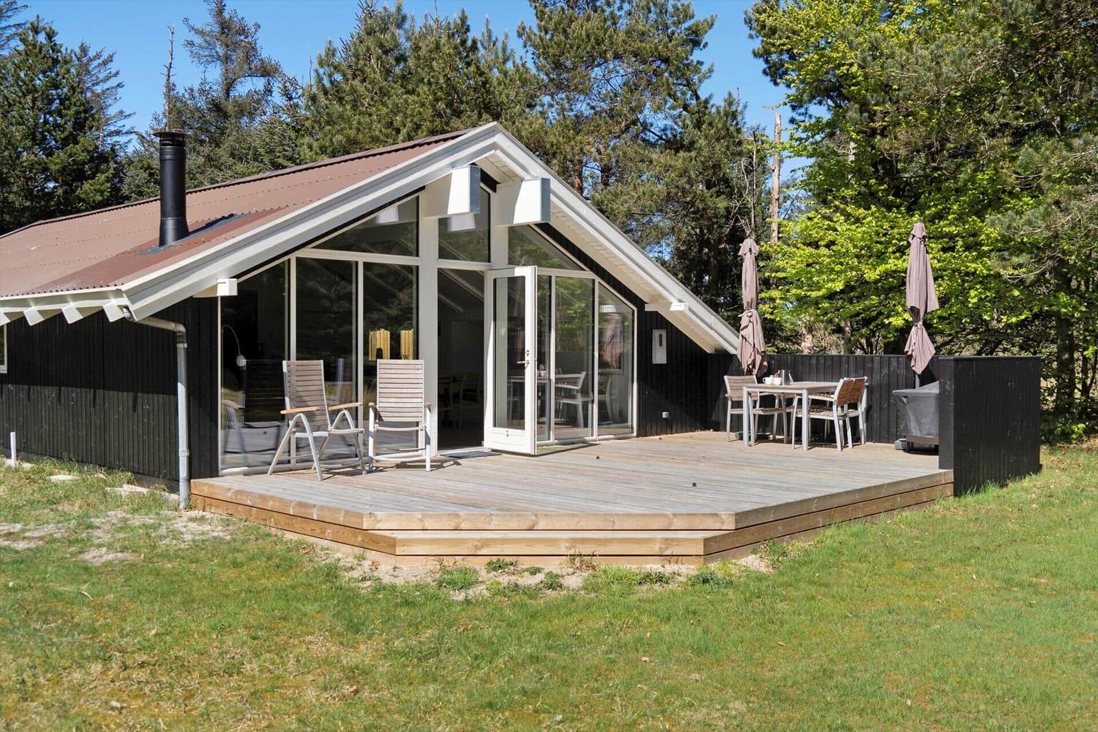 Moderne Hütte mit großem Holzdeck, Sitzgelegenheiten und Grillplatz im Grünen.