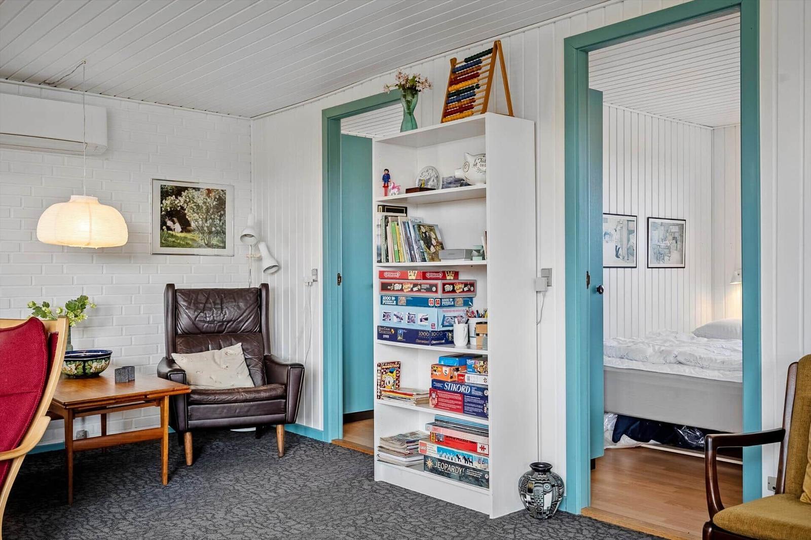 Living room with bookcase, leather armchair, and view into bedroom with bed.