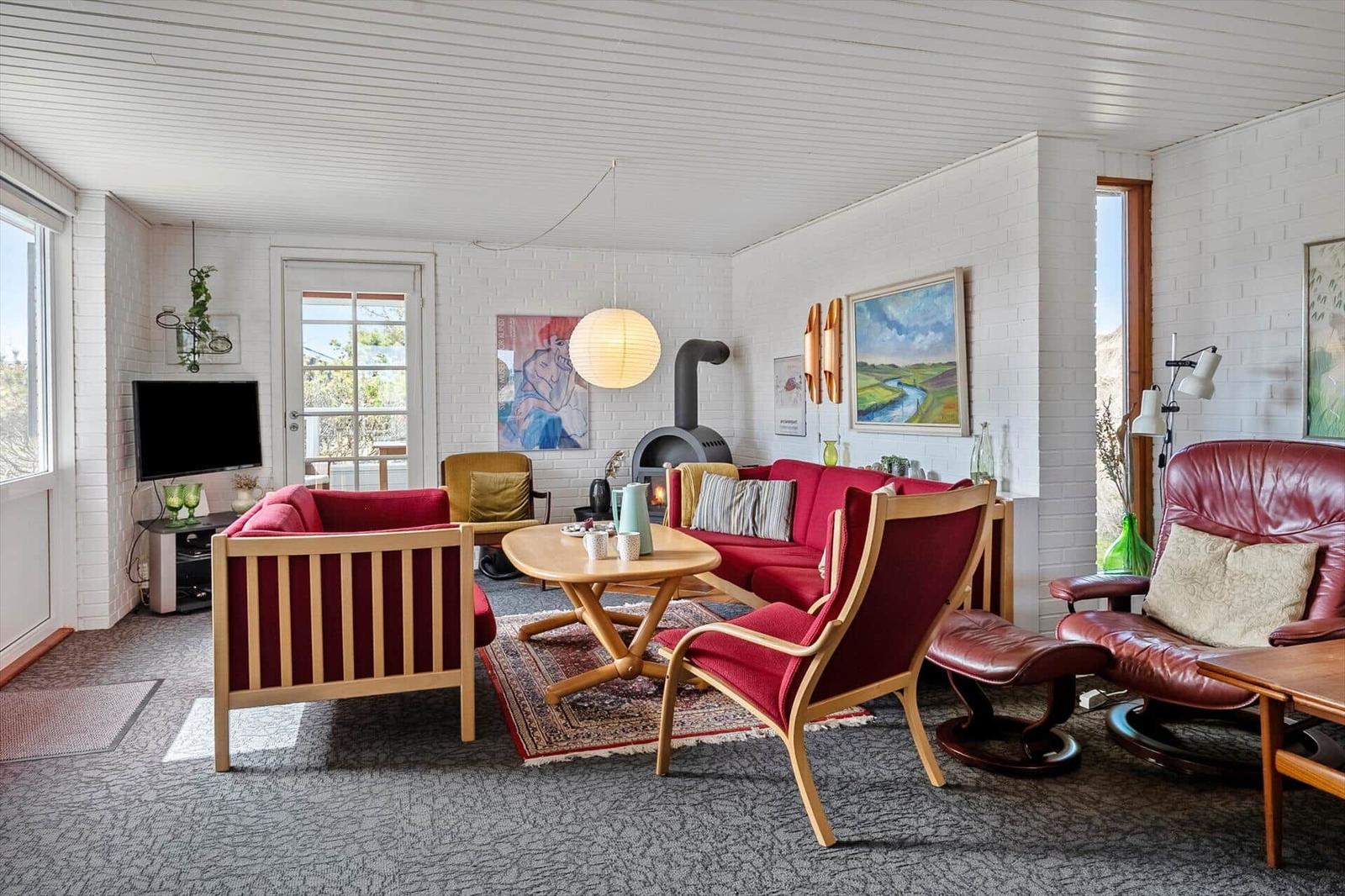 Living room with red sofa, wooden furniture, and fireplace. White walls, large windows, and wall art.