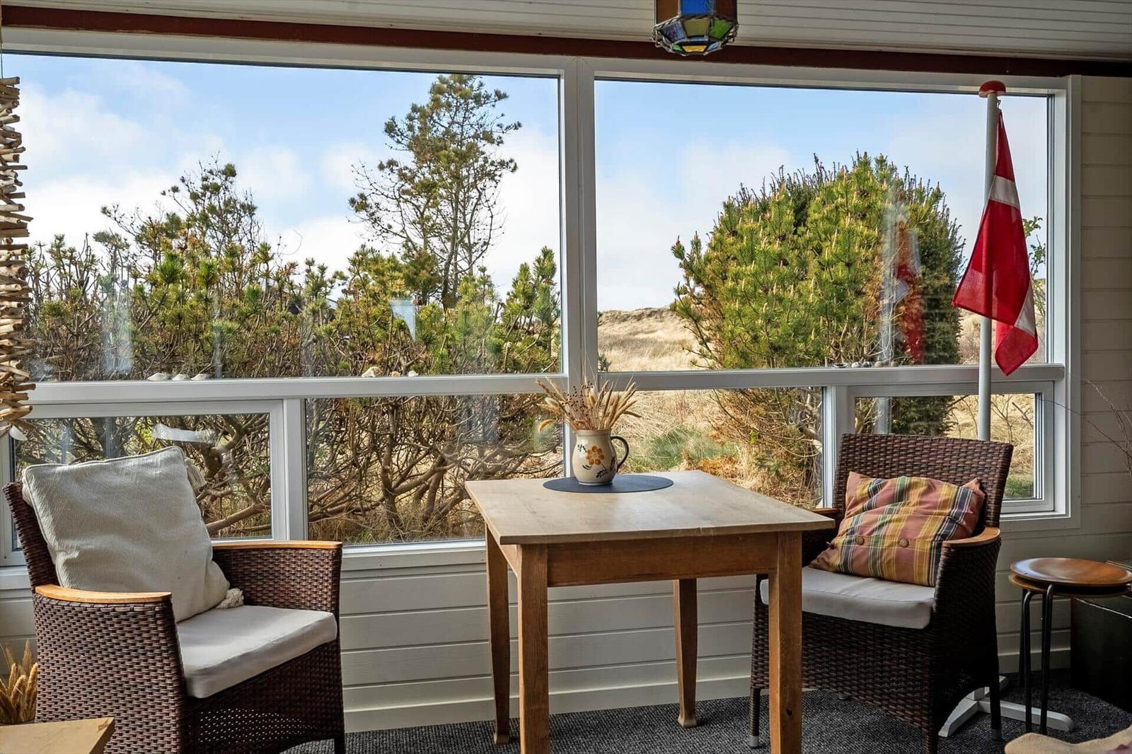 A table with two chairs in front of large windows with a view of trees and a flag.