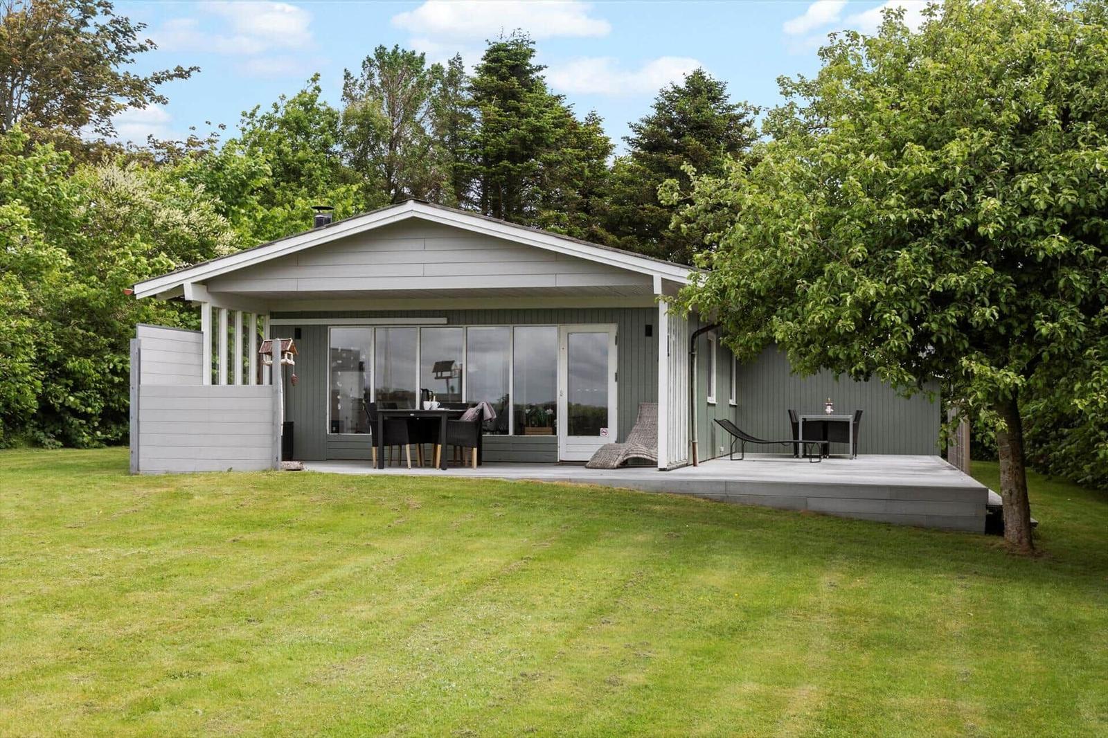 Moderne Hütte mit Terrasse, Garten und Bäumen im Hintergrund.