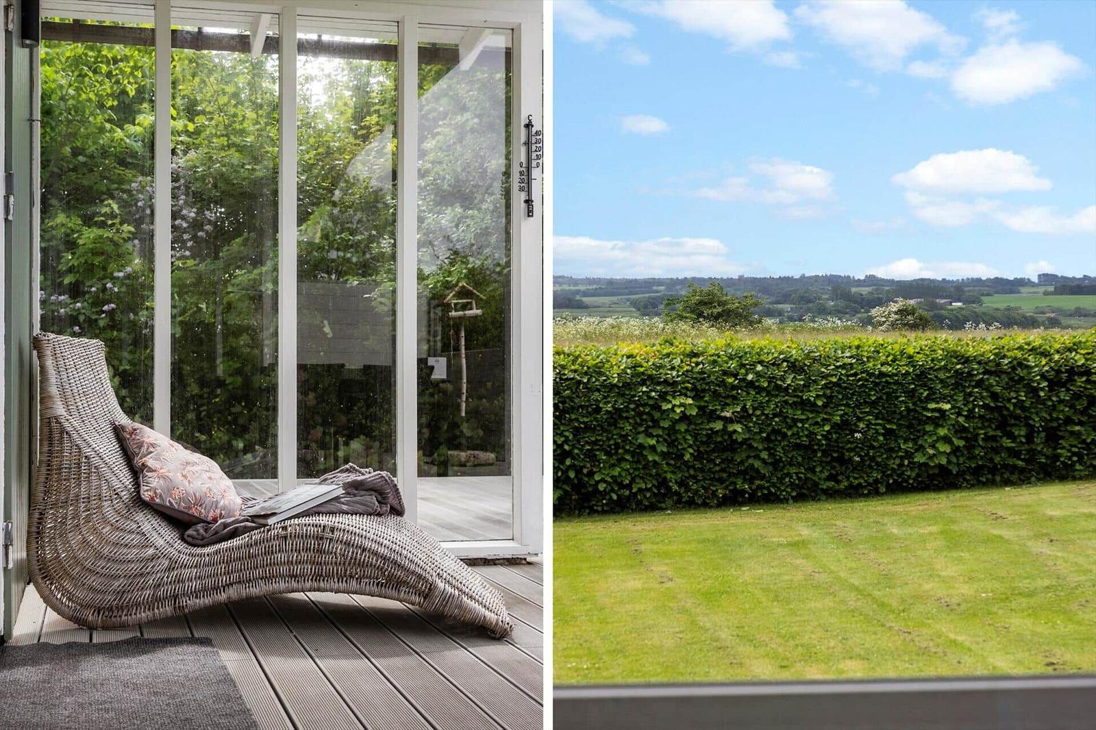 Wickerliege auf Terrasse mit Blick auf grünen Garten und Landschaft.