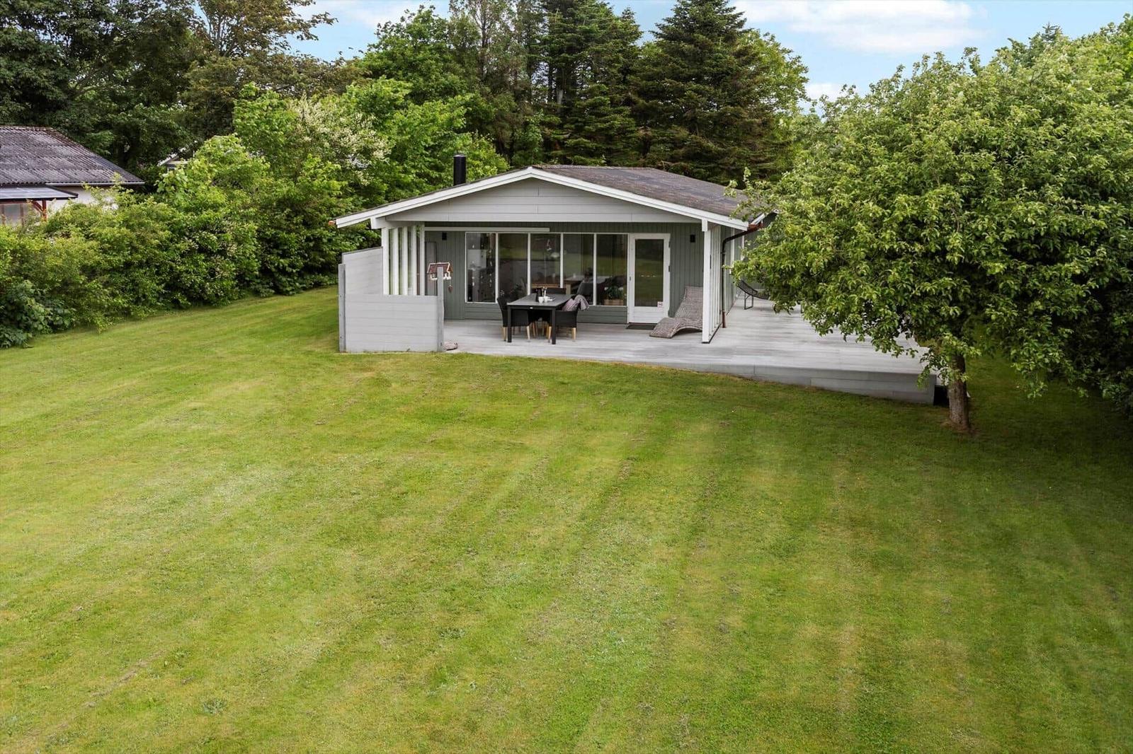 Ein Haus mit Terrasse, Garten und Bäumen im Hintergrund.