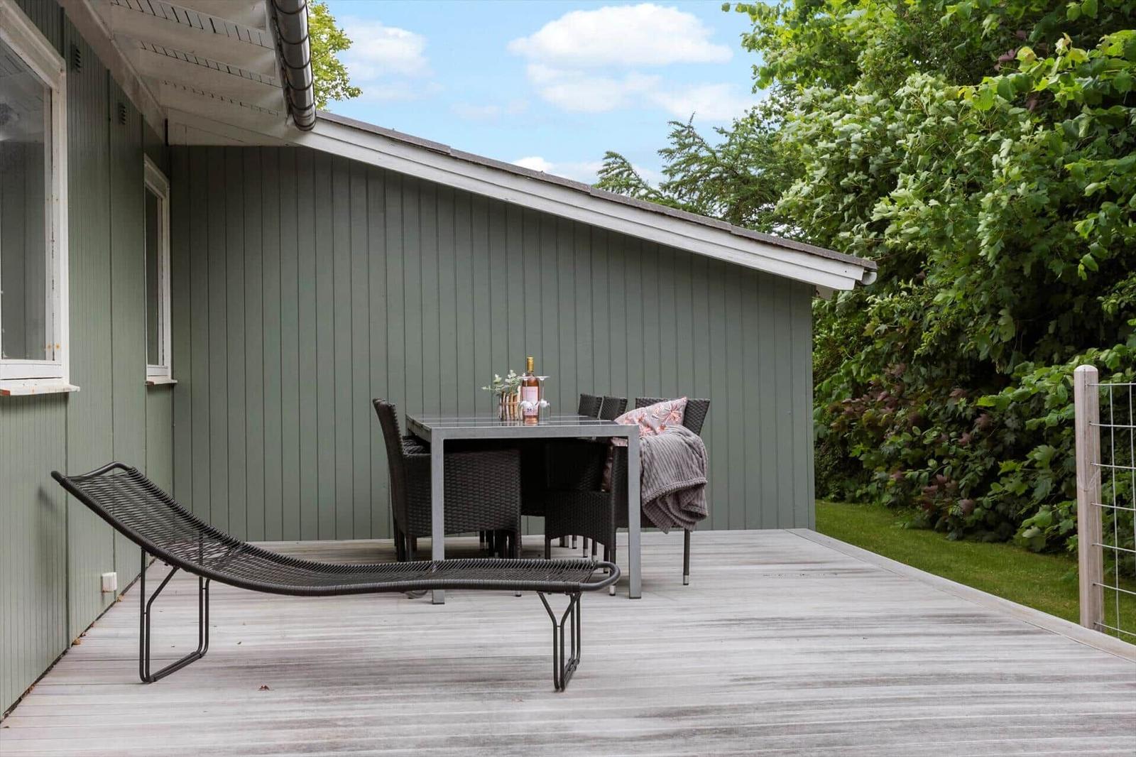 Terrasse mit Liegestuhl, Tisch und Stühlen neben grünem Haus.
