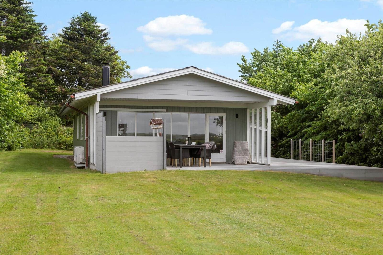 Ein Haus mit Terrasse und Garten. Es hat große Fenster und einen Grillplatz.
