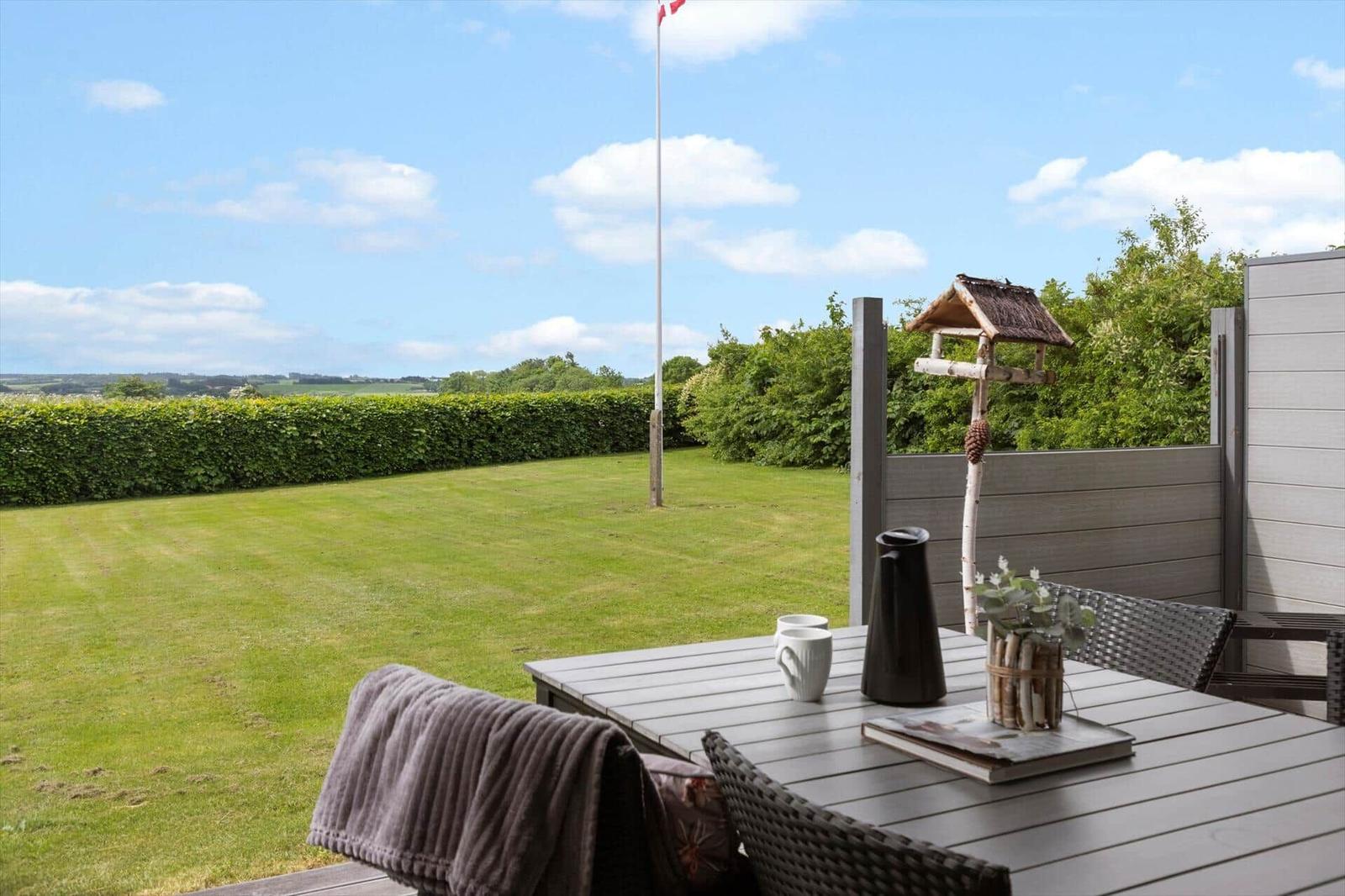 Terrasse mit Tisch, Stühlen und Blick auf grünen Rasen und Hecke.