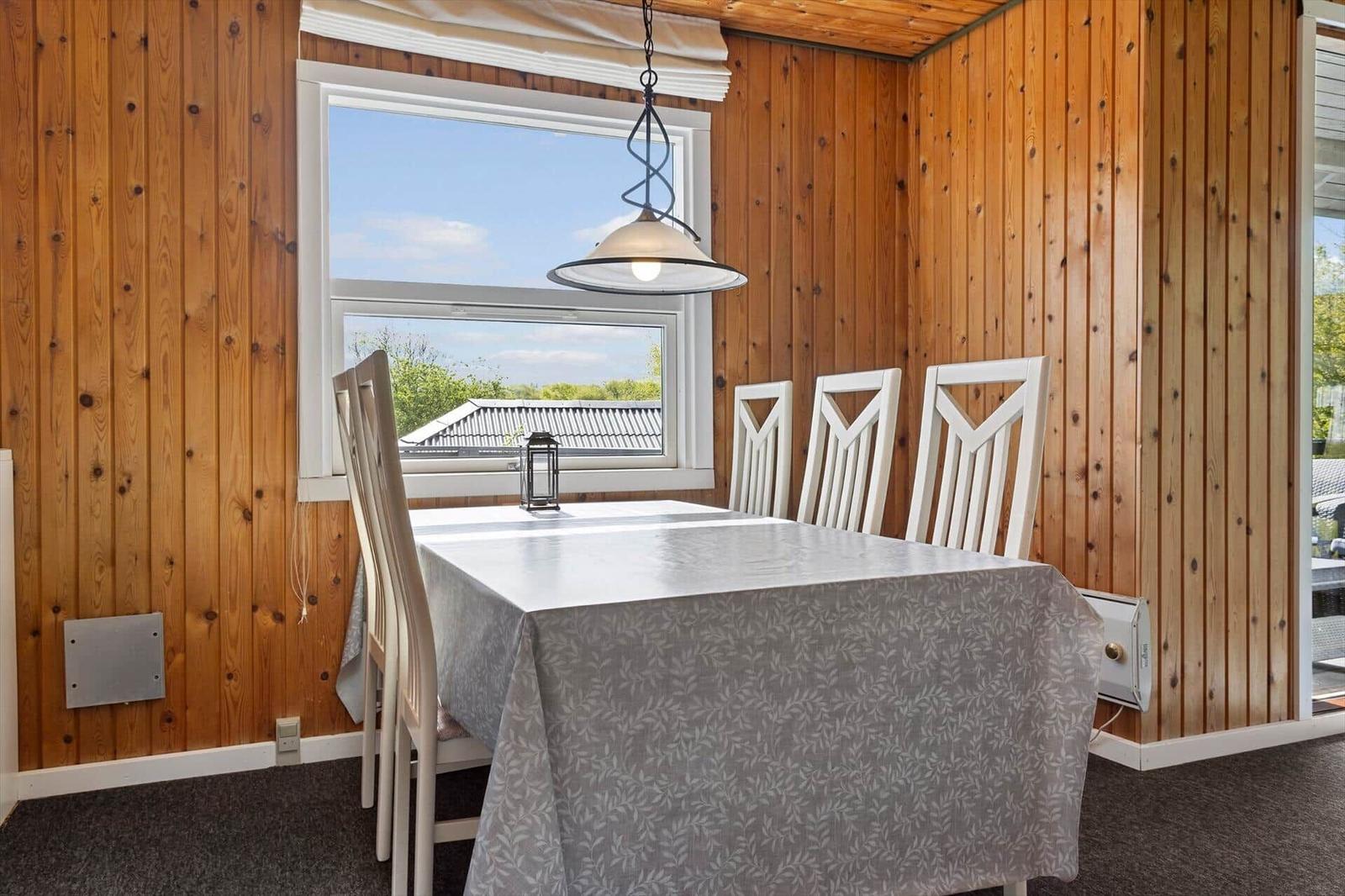 Esszimmer mit Holzwänden, Tisch mit Tischdecke und Fensterblick.