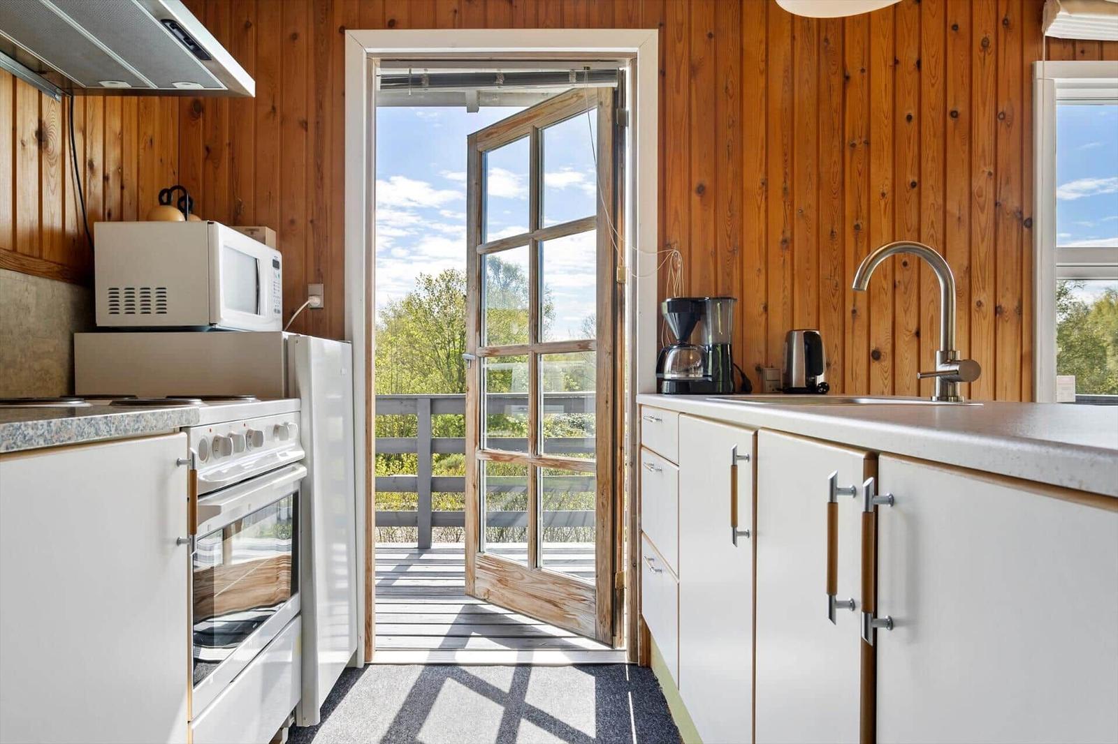 Küche mit Holzwand, Tür zum Balkon und Küchengeräten.