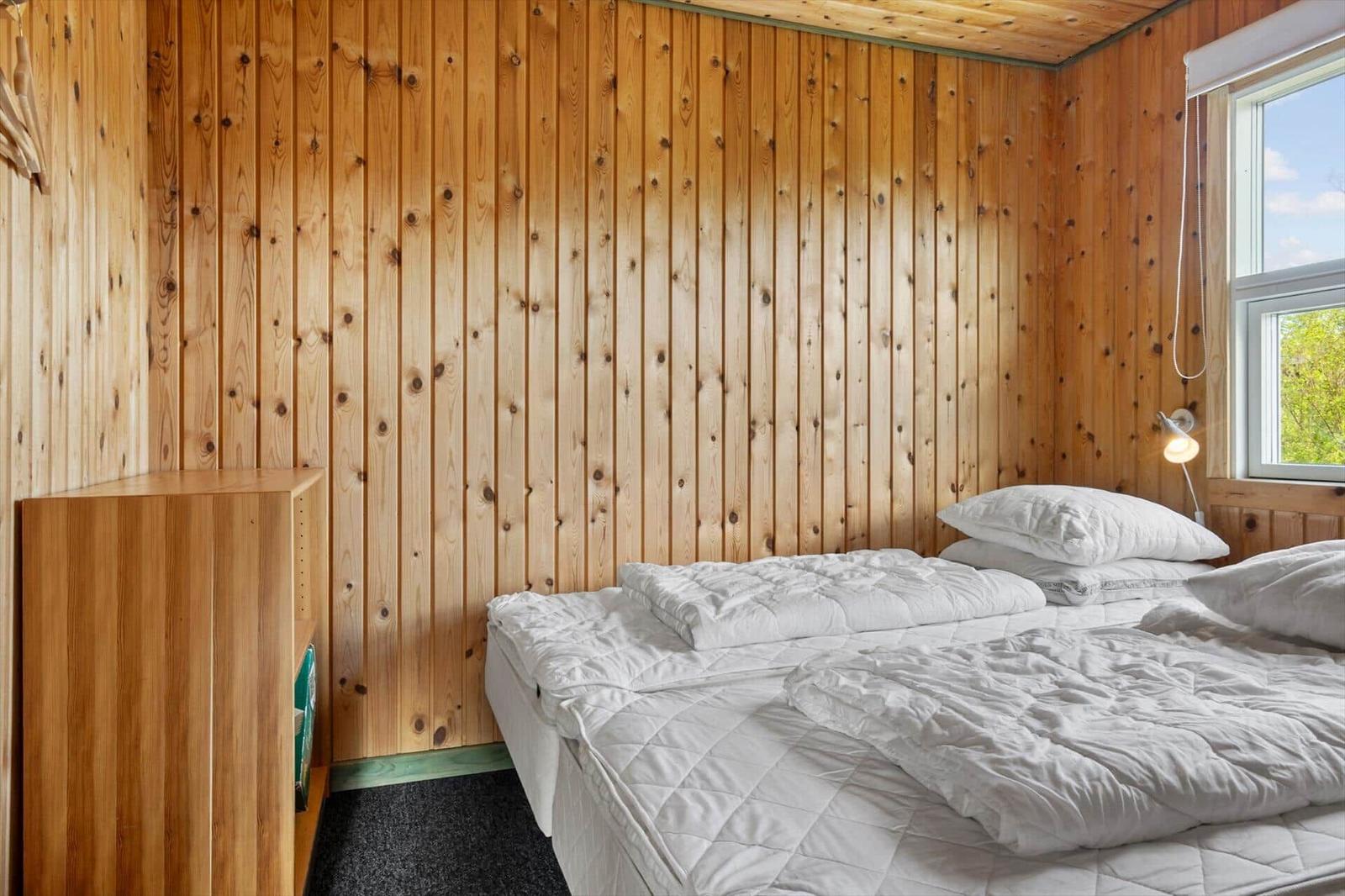 Schlafzimmer mit Holzwand, Bett und Fenster