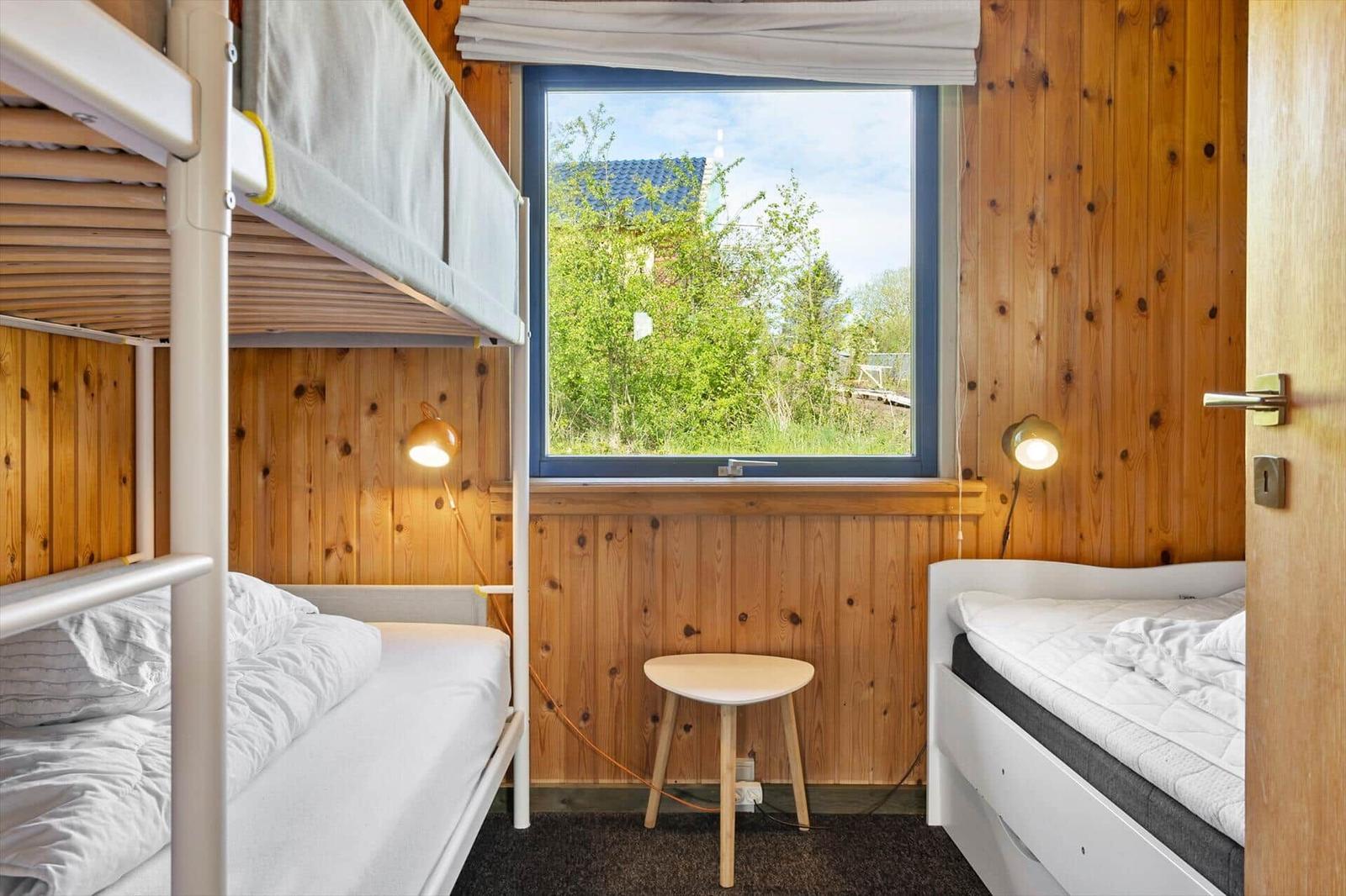 Zimmer mit Etagenbett, Einzelbett und Fensterblick auf Grünflächen.