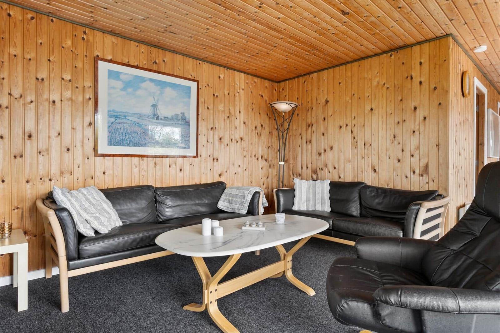 Wohnzimmer mit Holzwänden, schwarzen Ledersofas und ovalen Tisch.