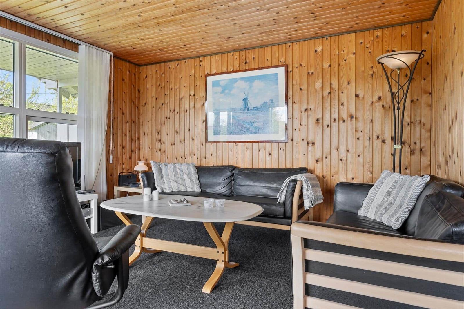 Wohnzimmer mit Holzwänden, Sofa, Couchtisch und Fenster. Wandbild zeigt Windmühle.