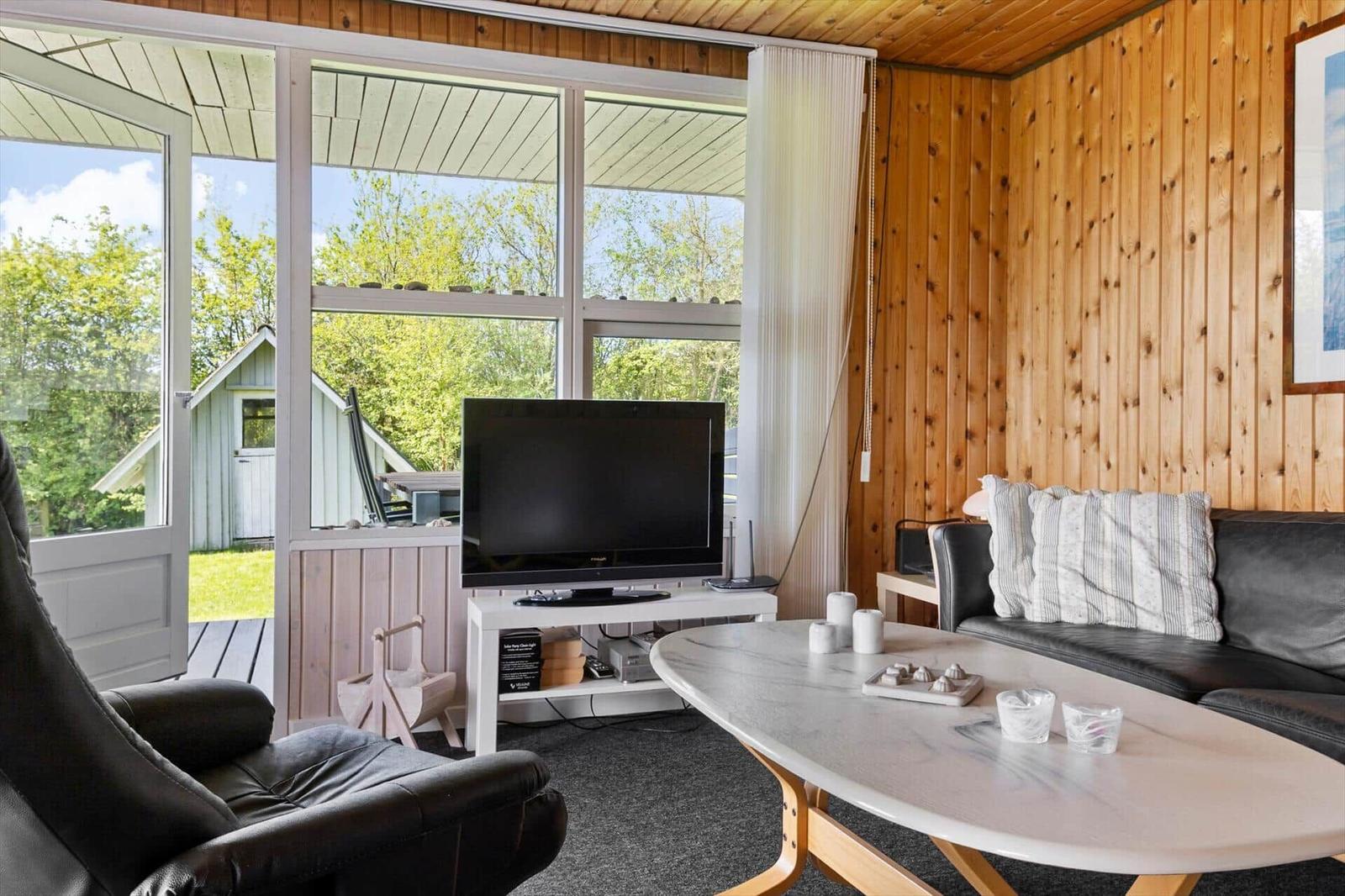 Wohnzimmer mit Sofa, Fernseher und großem Fensterblick auf Garten.