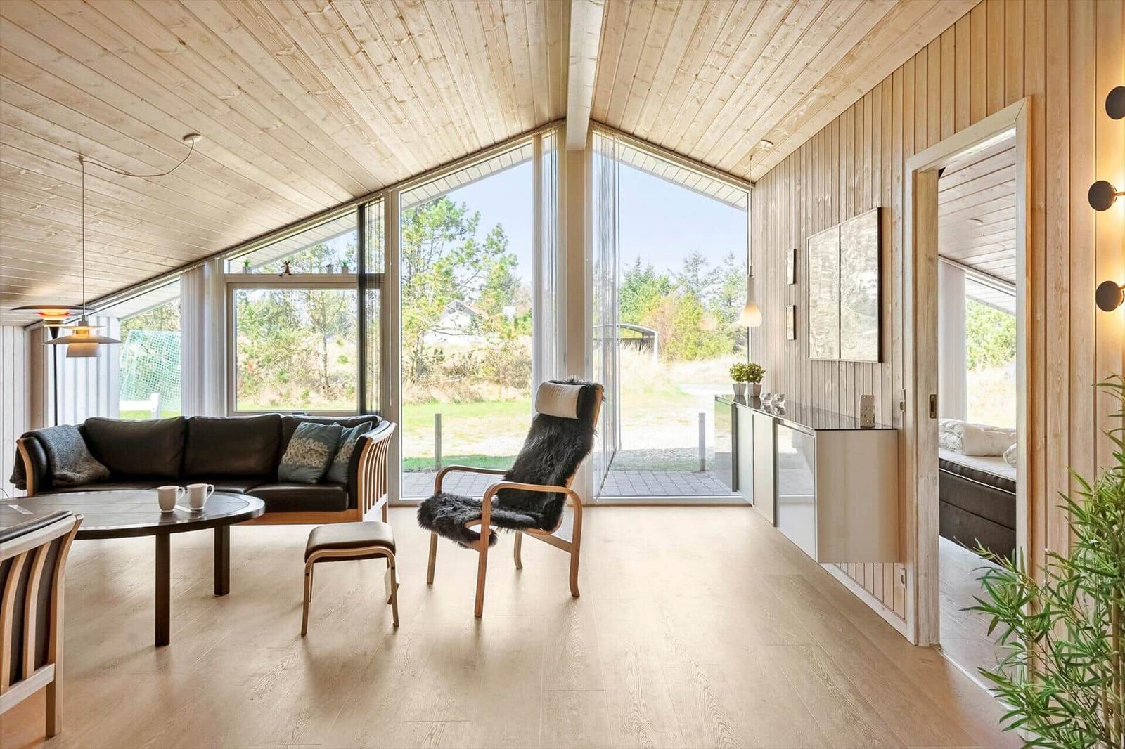 Wohnzimmer mit Holzdecke, großen Fenstern und Sitzgelegenheiten.