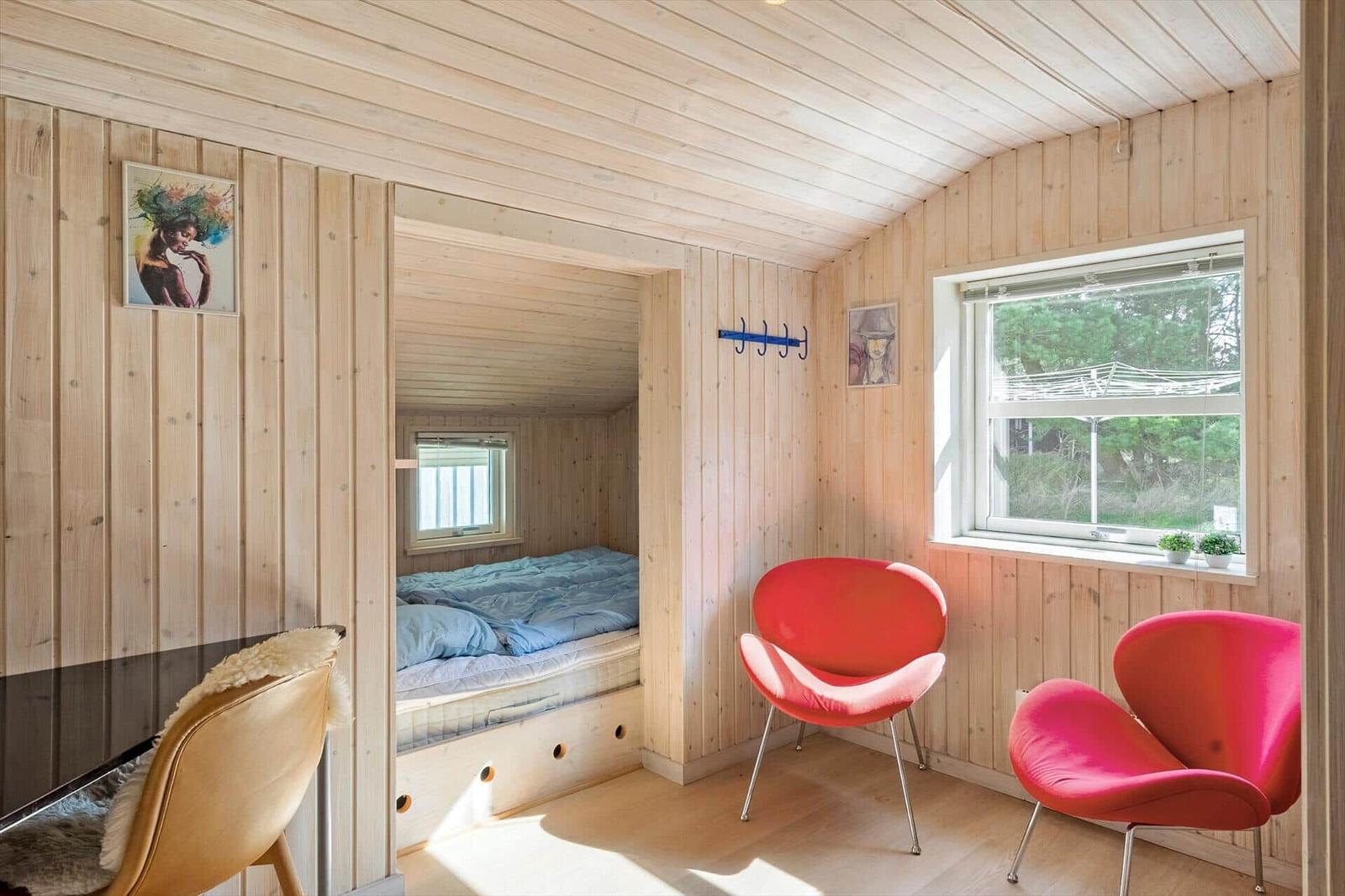 Ein Raum mit Holzwänden, zwei roten Stühlen und einem Bett im Anbau.