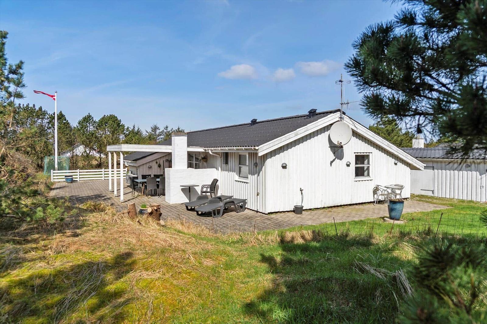 Wohnhaus mit Terrasse, Liegestühlen und Satellitenschüssel. Umgeben von Gras und Bäumen.
