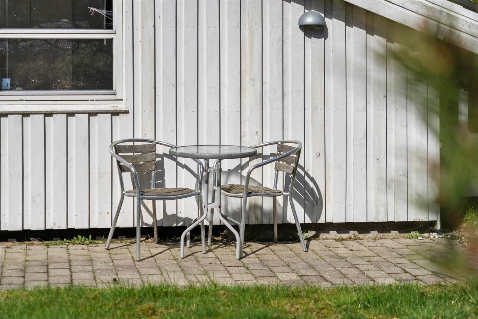 Außenbereich mit Tisch und zwei Stühlen vor weißer Holzwand