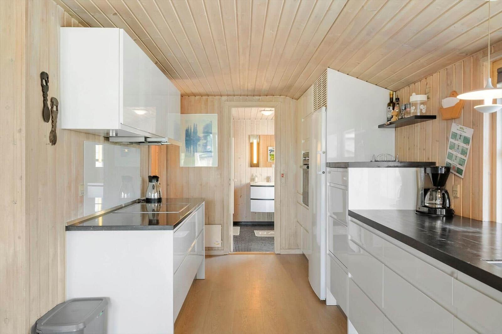 Moderne Küche mit weißen Schränken und dunklen Arbeitsplatten. Holzwände und -boden.