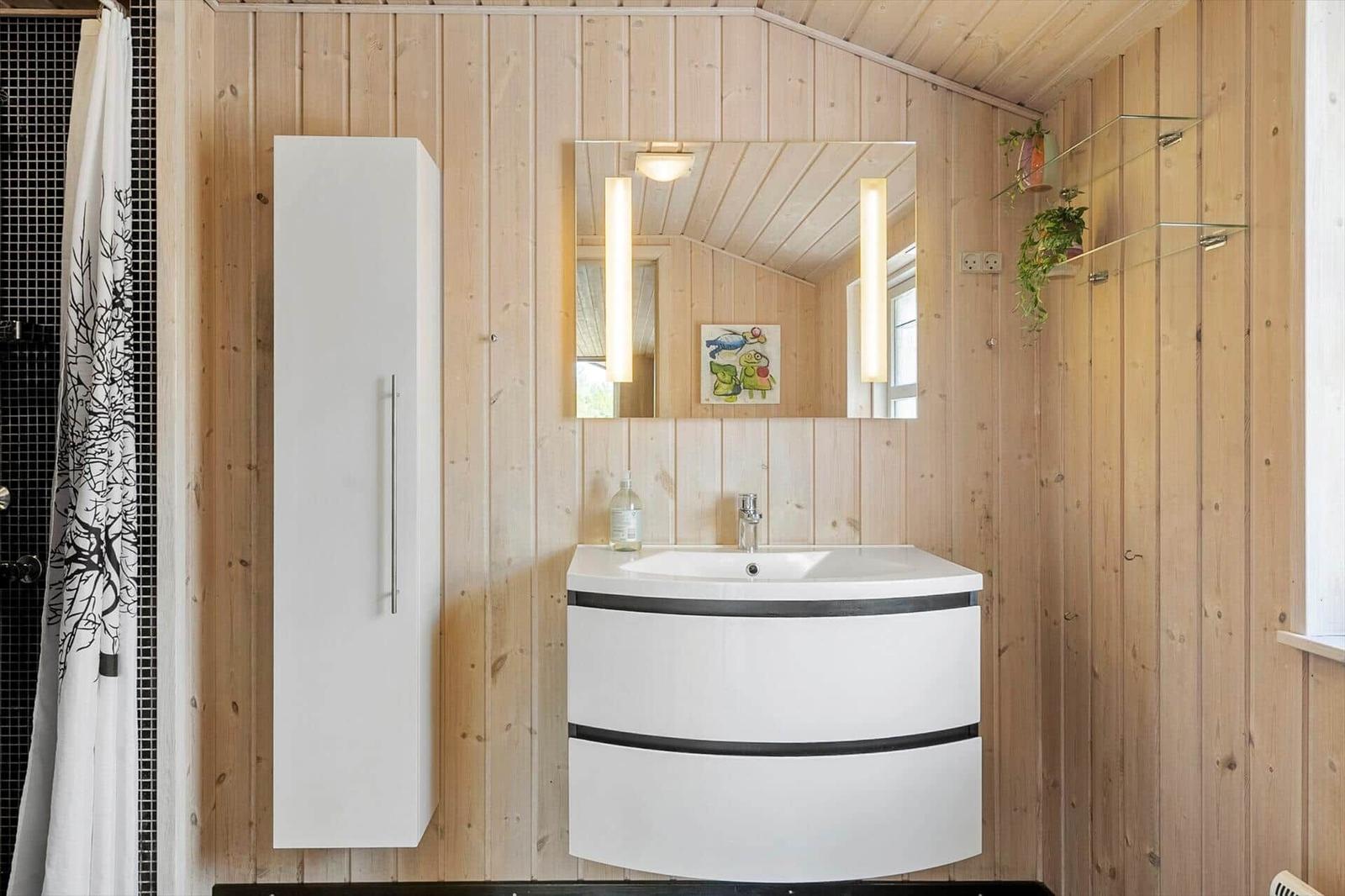 Badezimmer mit Holzwand, Waschbecken, Spiegel und Dusche mit Vorhang.