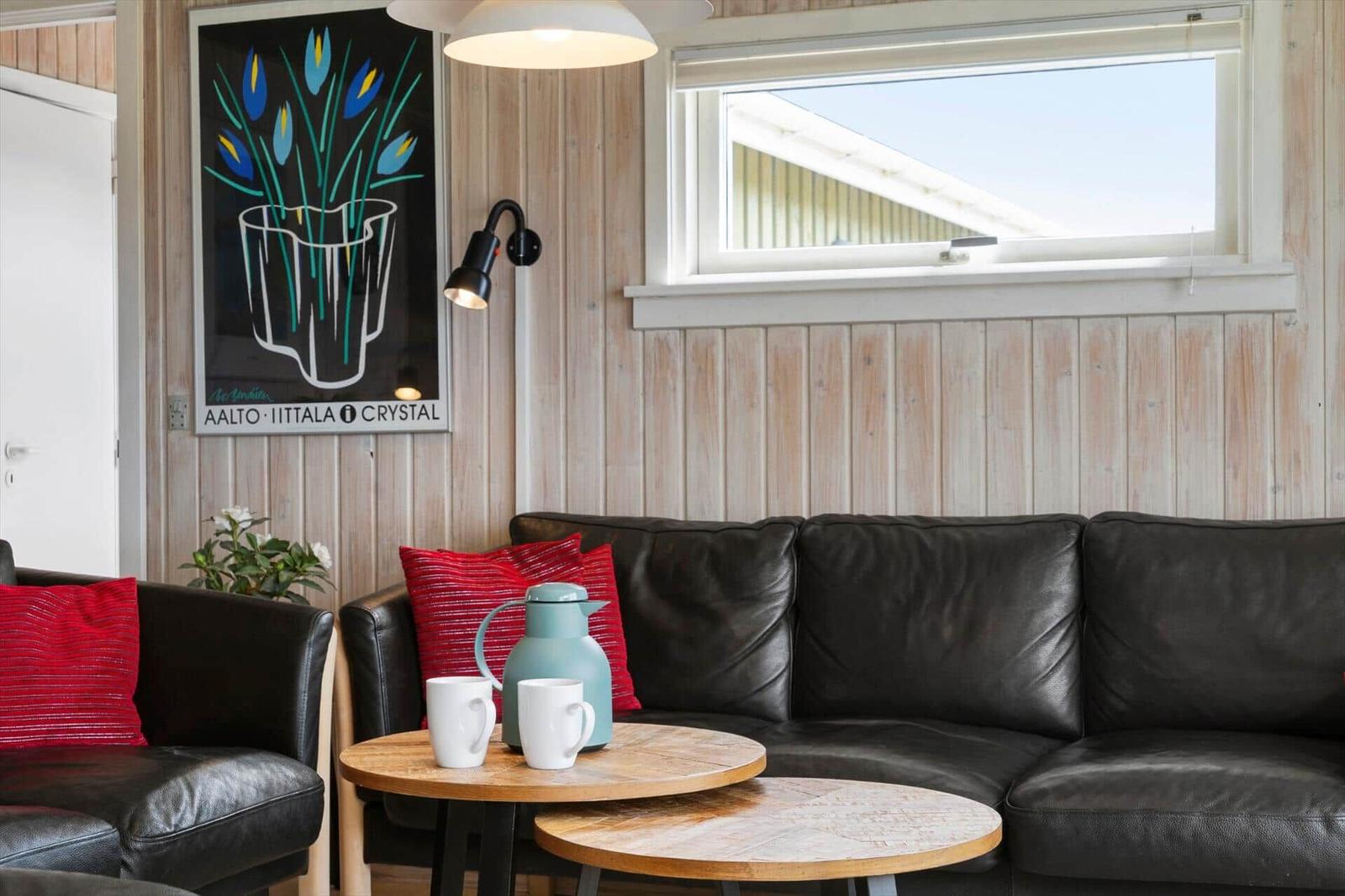 Black leather sofa with red cushions, wooden tables, and wall art on wood paneling.