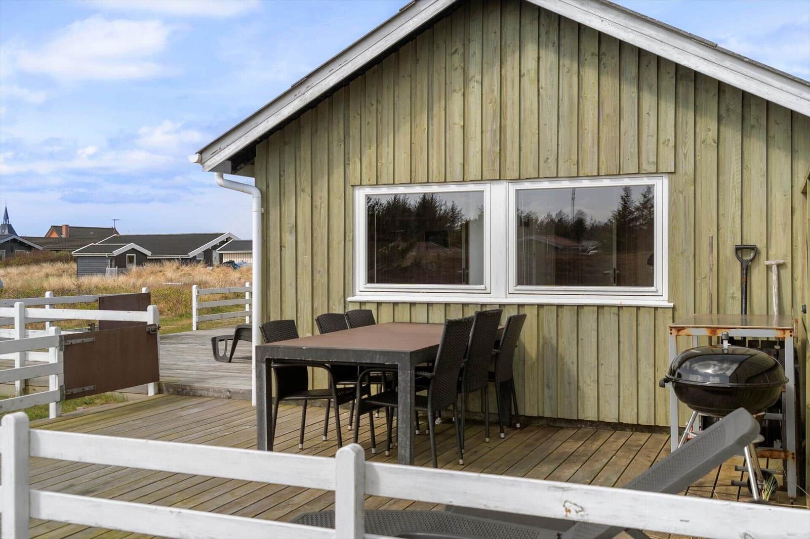 Deck with table, chairs, and grill beside wooden houses