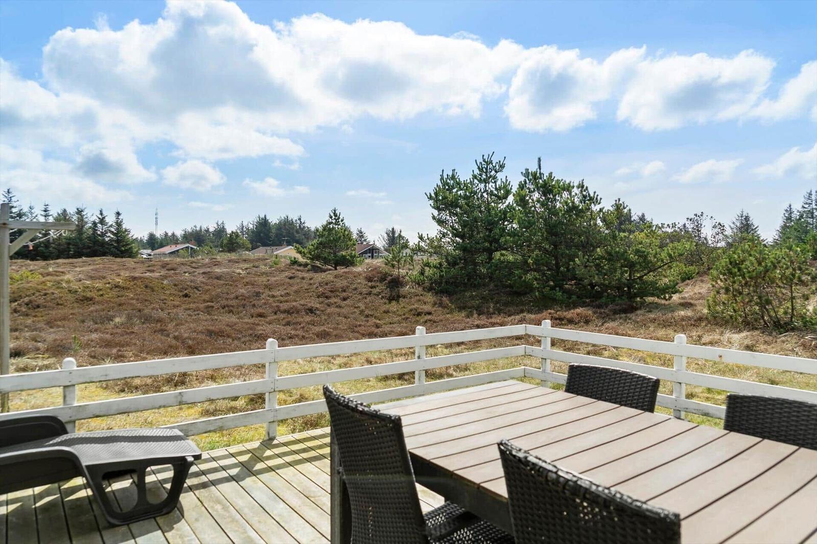 Deck with table and chairs, view of meadows and trees under blue sky.