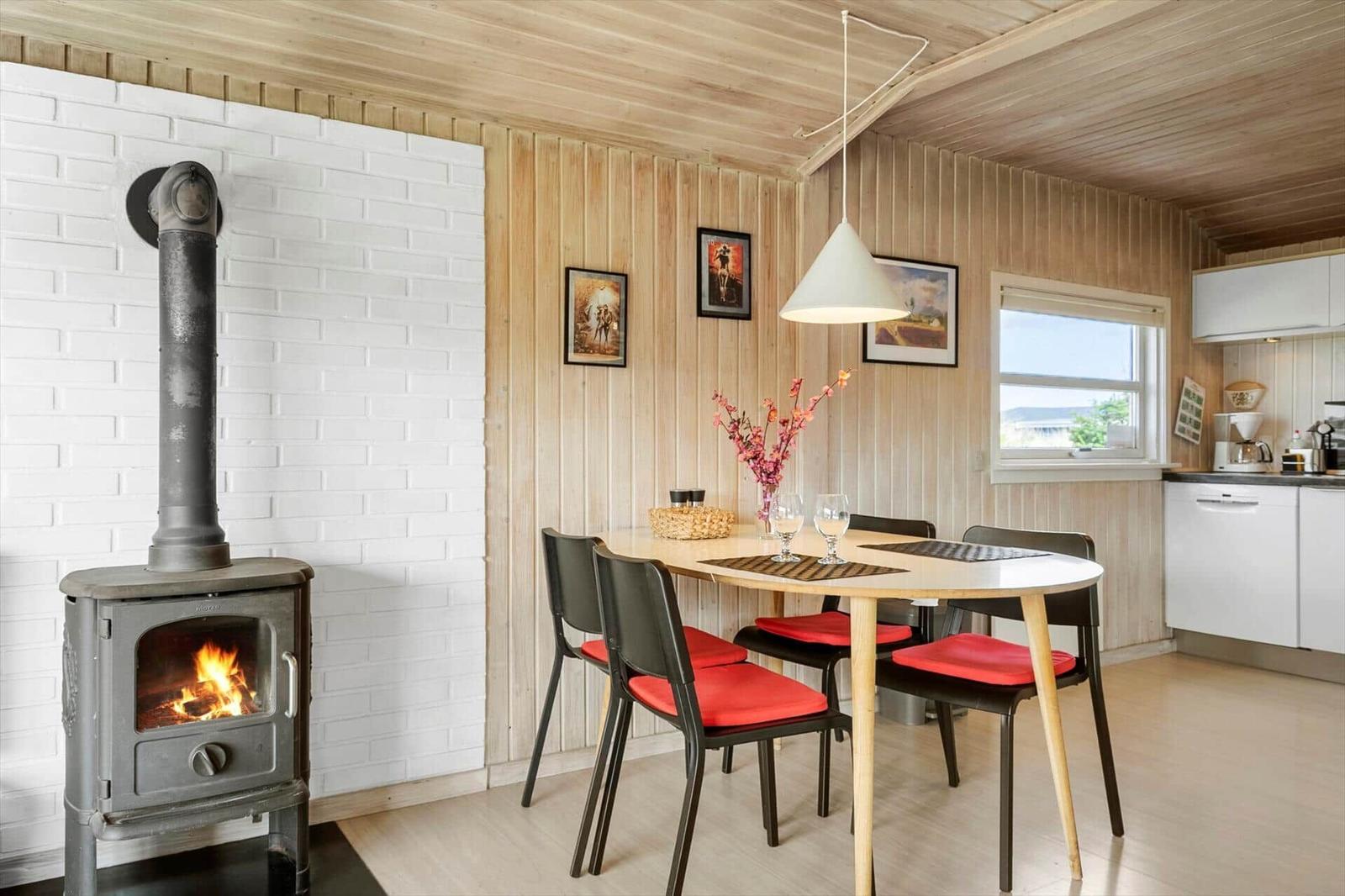 Dining area with table, chairs, and wood stove against white brick wall.