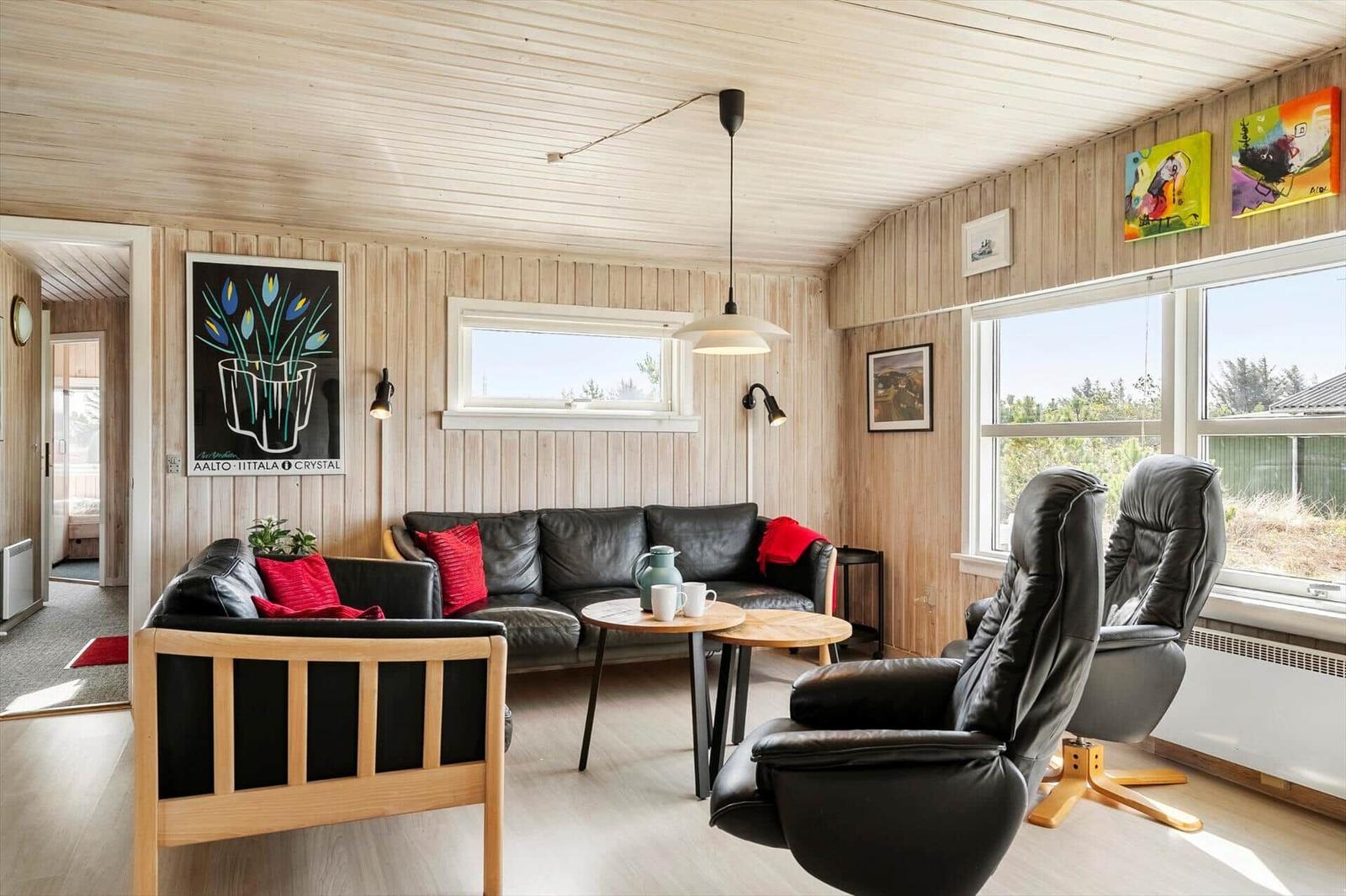 Living room with leather sofa, two chairs, and wood paneling on walls and ceiling.