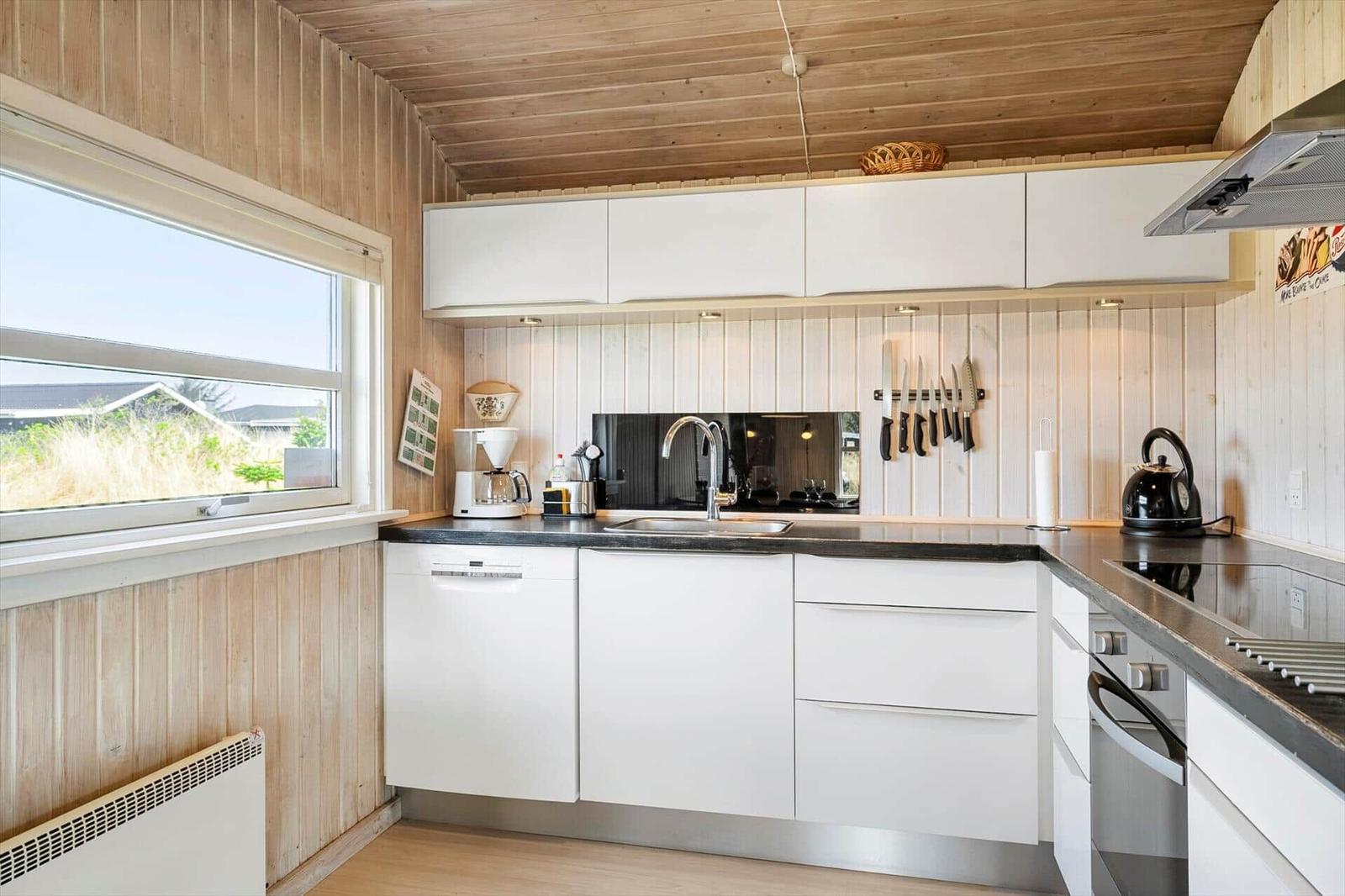 Kitchen with white cabinets, dark countertop, and wooden walls. Window with view outside.