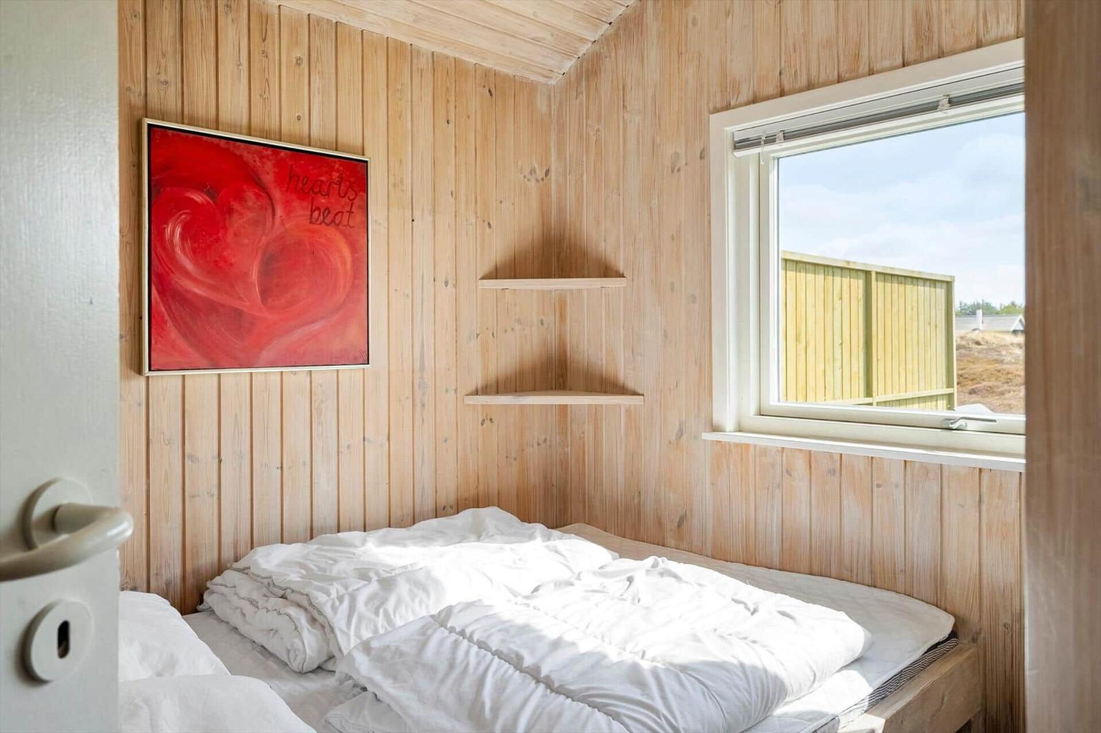 Bedroom with wooden walls, bed, and window. A painting hangs on the wall.