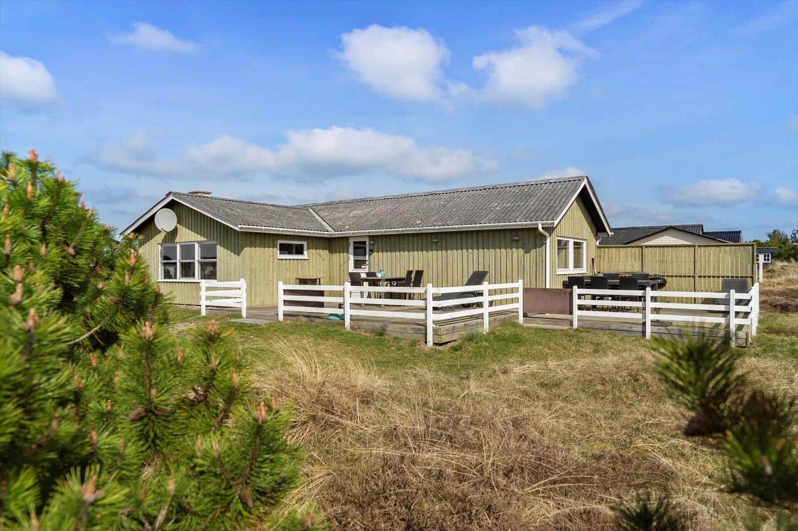 A wooden house with terrace, garden, and white fence under blue sky.