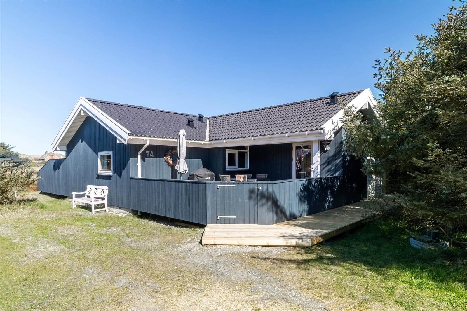 Ein blau gestrichenes Ferienhaus mit Terrasse und Garten. Weiße Bank und Grill sind vorhanden.