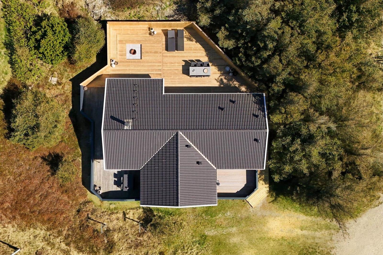 Haus mit Holzterrasse und Garten, umgeben von Bäumen und Grasflächen.