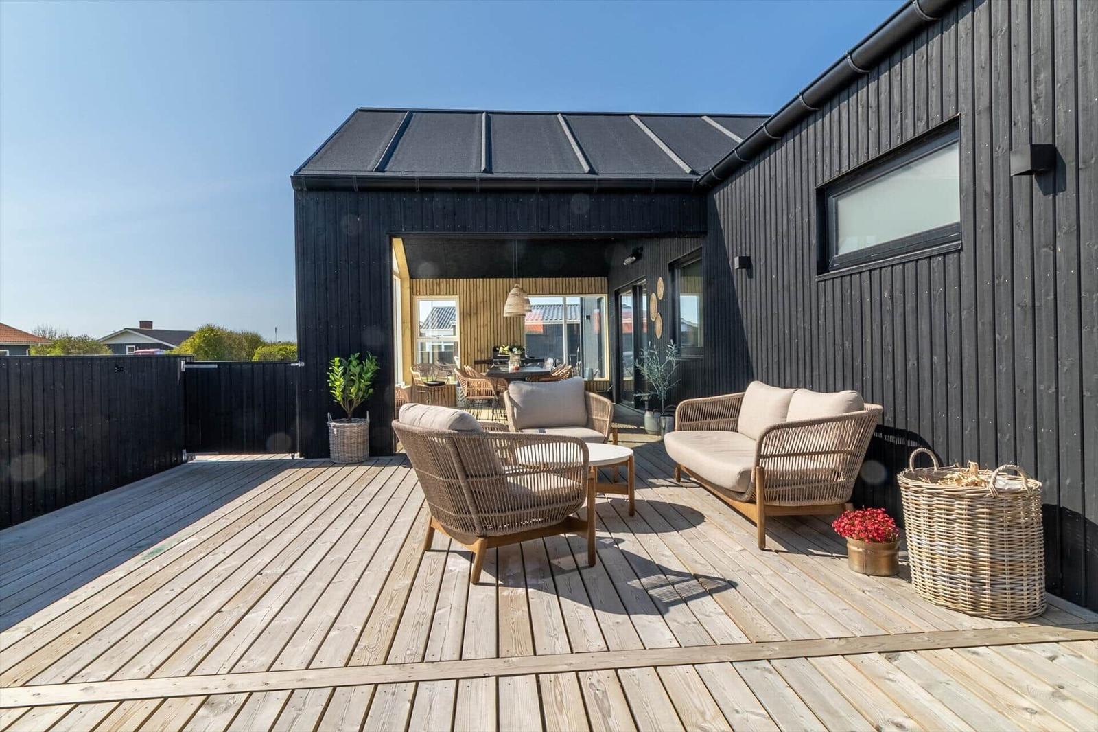 Terrasse mit Sitzgelegenheiten und Blick in das Haus. Holzdeck und schwarze Fassade.