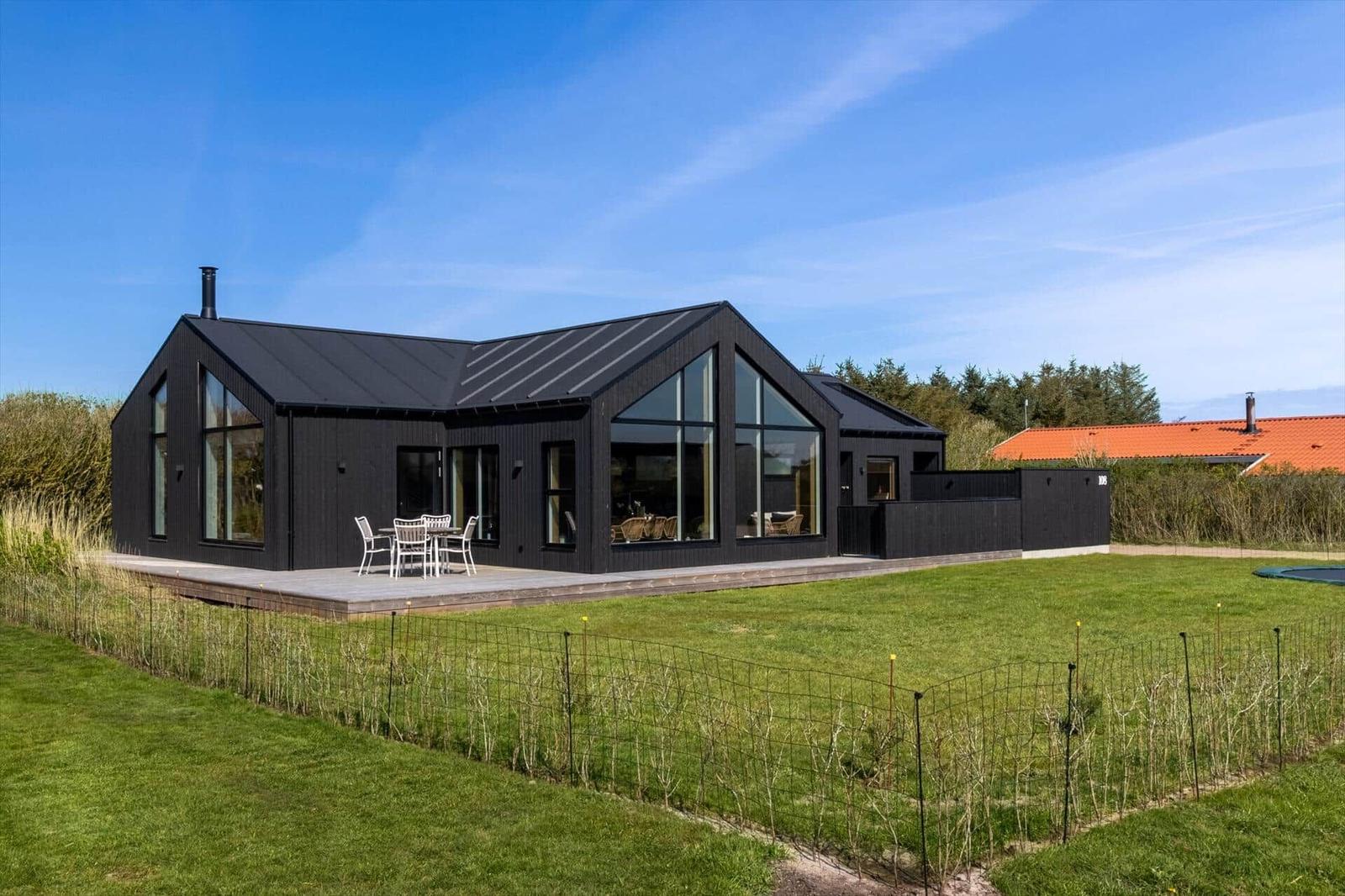 Moderne schwarze Villa mit großem Garten und Terrasse mit Tisch und Stühlen.