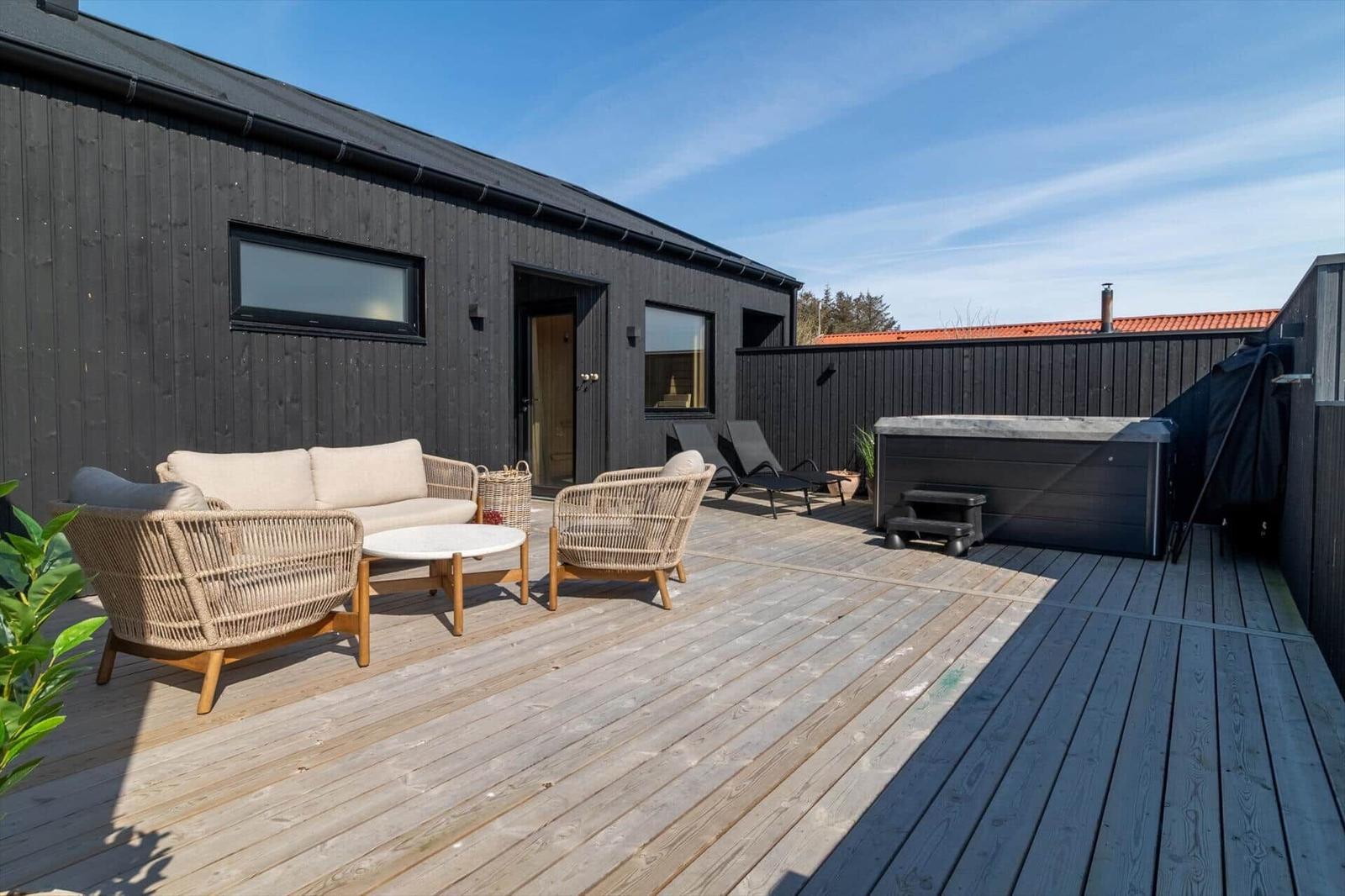 Terrasse mit Sofa, Stühlen und Whirlpool. Schwarzes Haus mit Holzdecke.