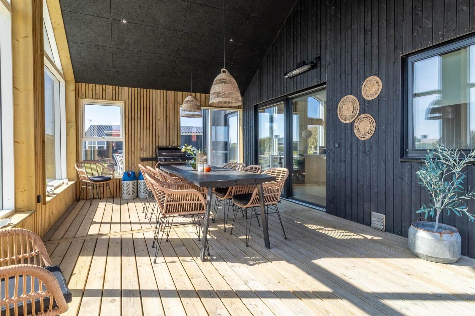 Terrasse mit Esstisch, Stühlen und Grill. Schwarze Holzwände und Holzdielen.