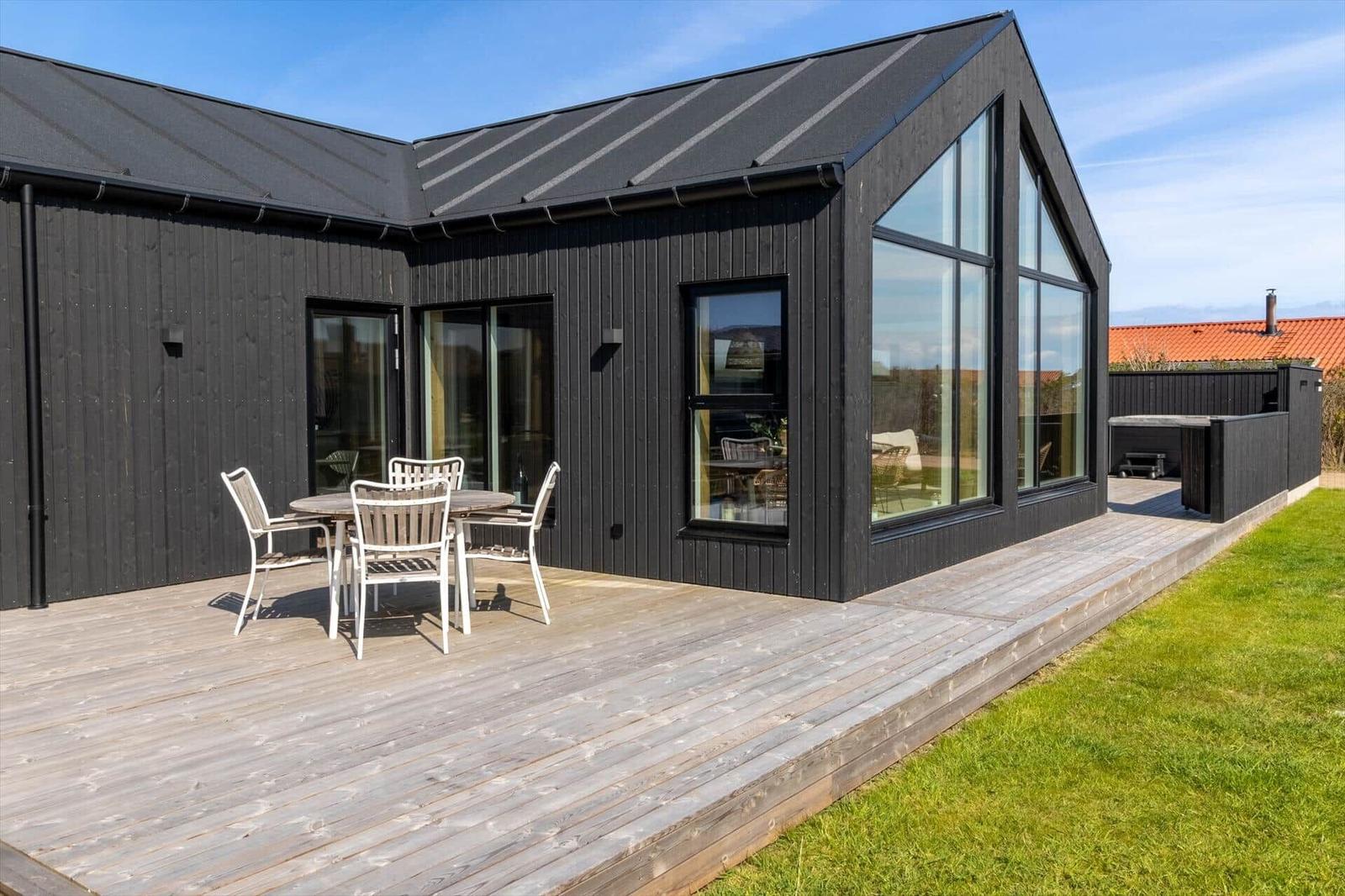 Moderne Villa mit Holzterrasse und großem Glasbereich. Außentisch mit Stühlen.