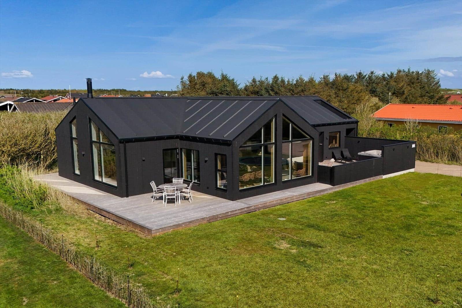 Moderne schwarze Villa mit großem Holzdeck und Garten. Große Fenster und Terrasse.