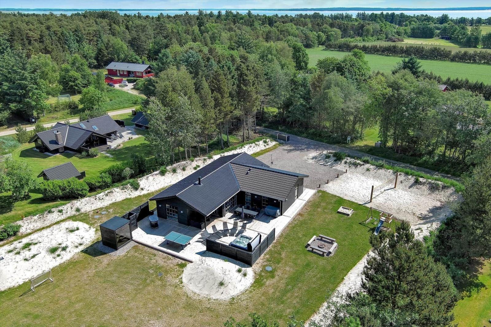 Modernes Haus mit Pool und Spielplatz in grüner Umgebung mit Wald und See.